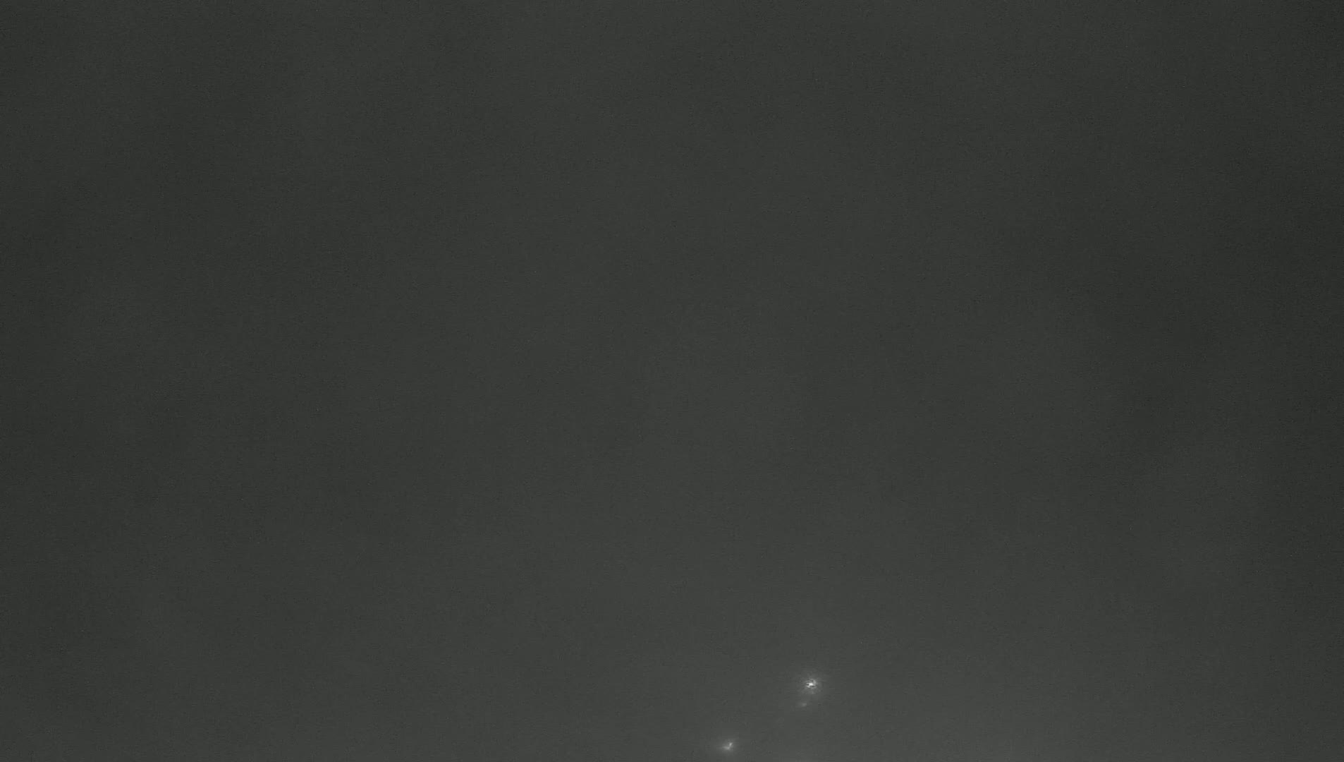 A dark gray, hazy sky shows two faint lights in the lower right corner.