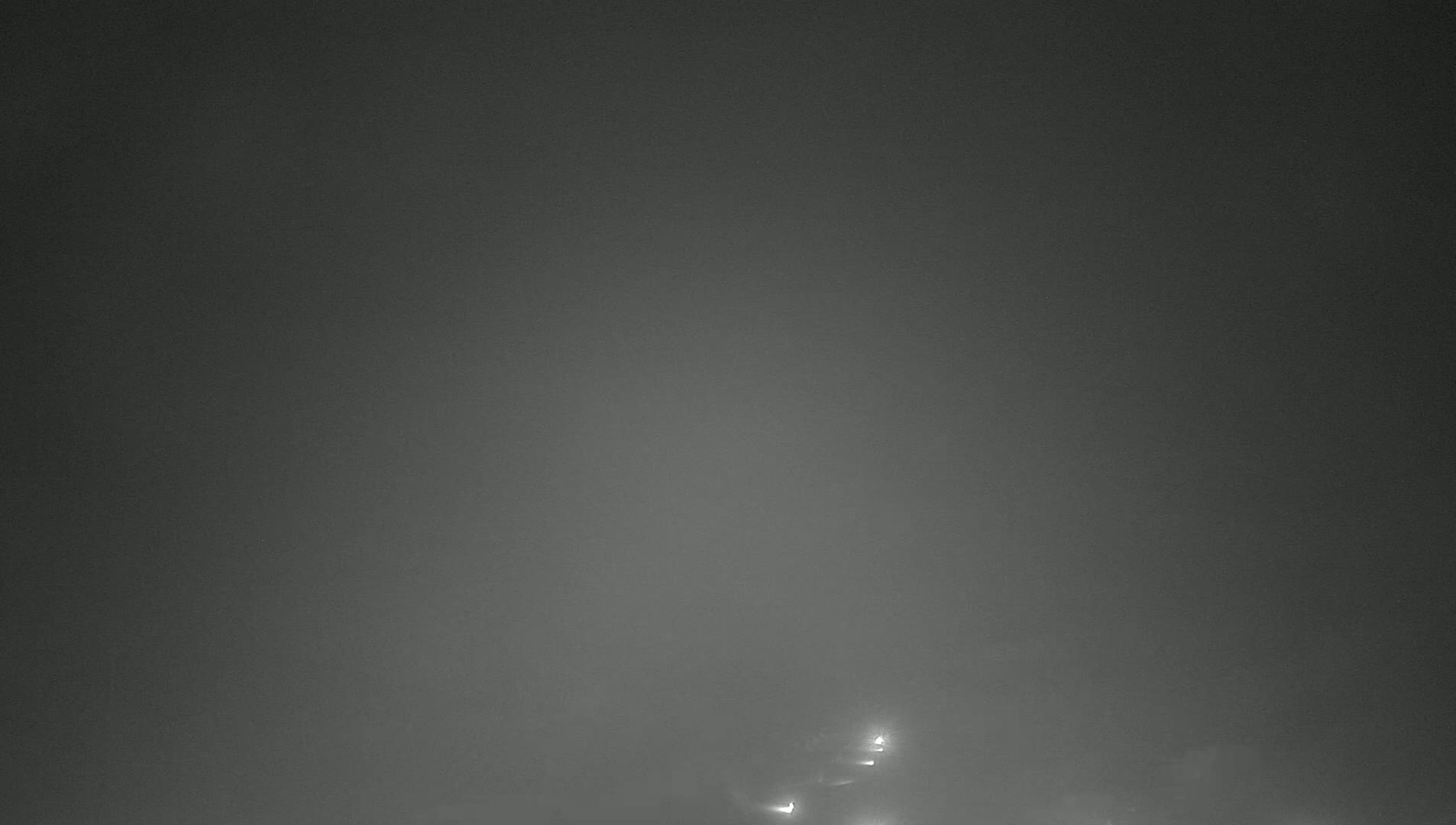 Faintly lit vehicles are visible through a thick fog at night.