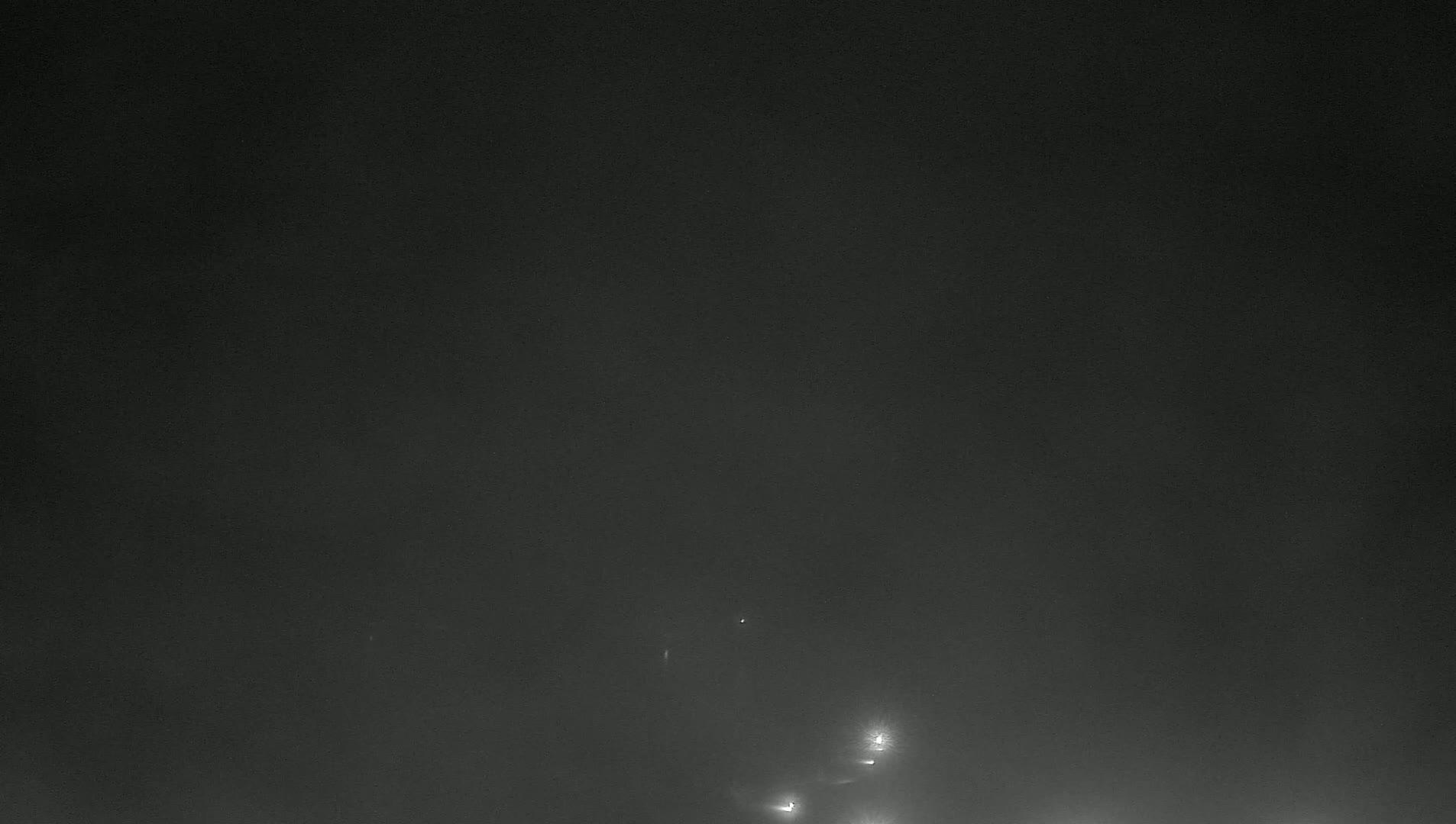 A dark, foggy scene at night shows faint lights in the lower section.