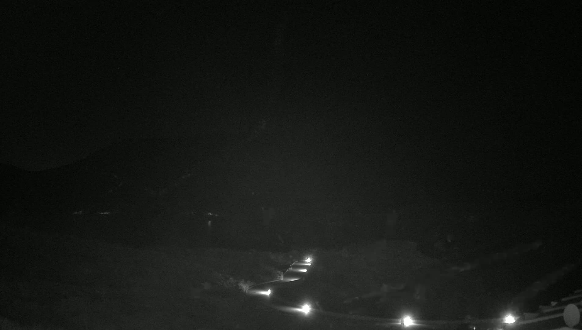 A dark, nighttime scene shows a curving road with dimly lit streetlights and a dark, hilly landscape in the background.