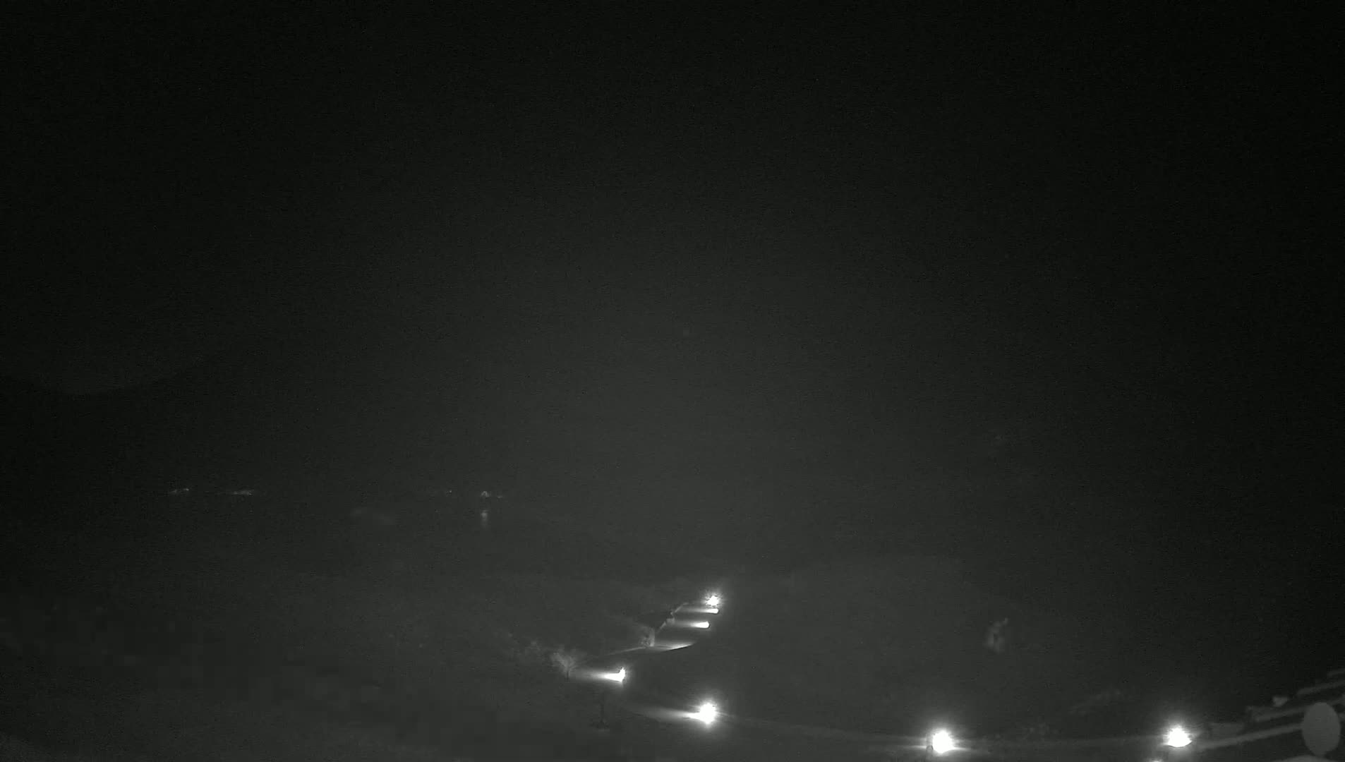 A dimly lit, winding road is visible at night under a dark sky.