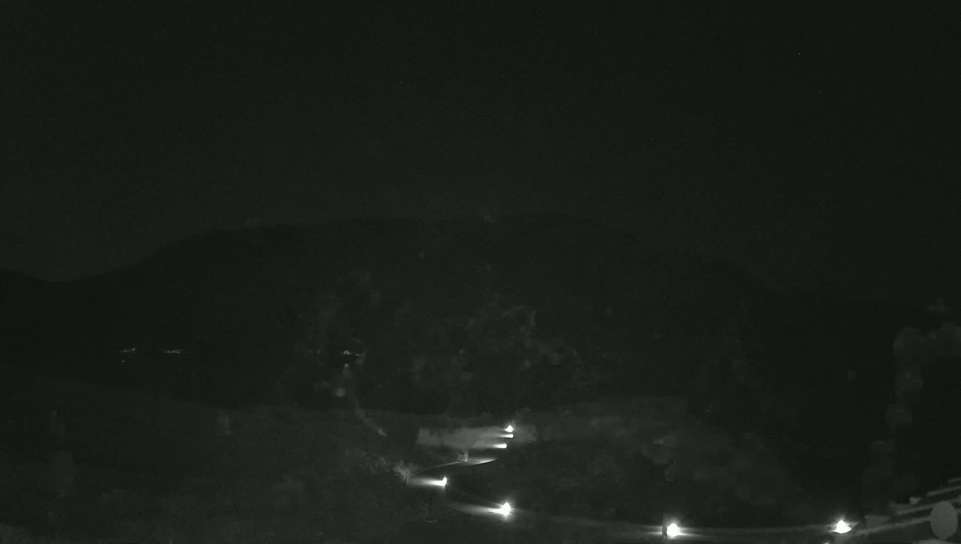 A winding road with dimly lit lights curves upward towards a dark mountain under a clear night sky.