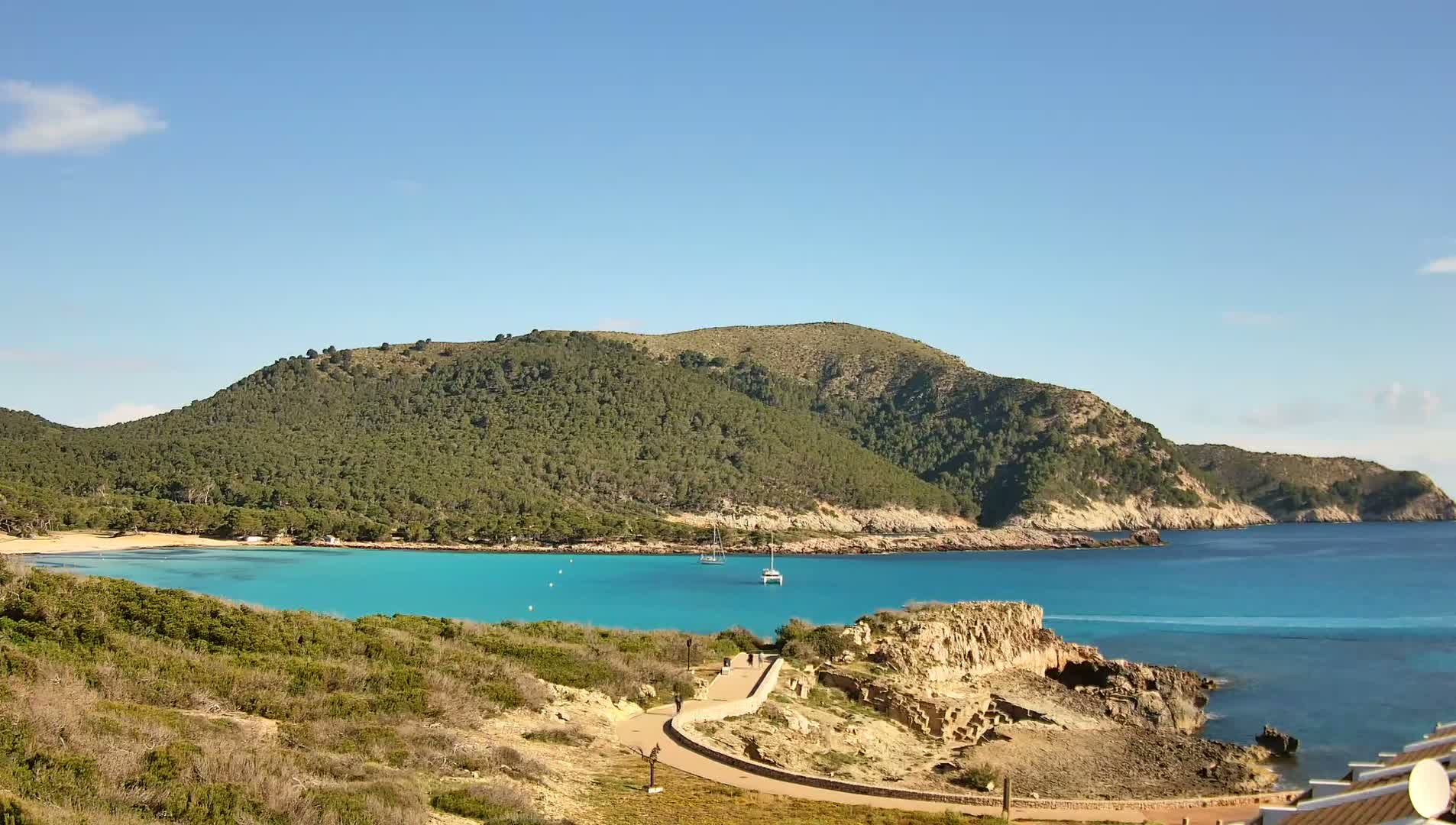 A secluded turquoise cove nestled in a rocky, tree-covered coastline on a sunny day.