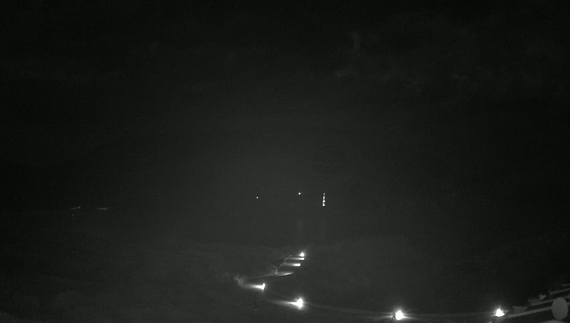 A dark, nighttime scene shows a winding road lit by a series of spaced-out lamps.