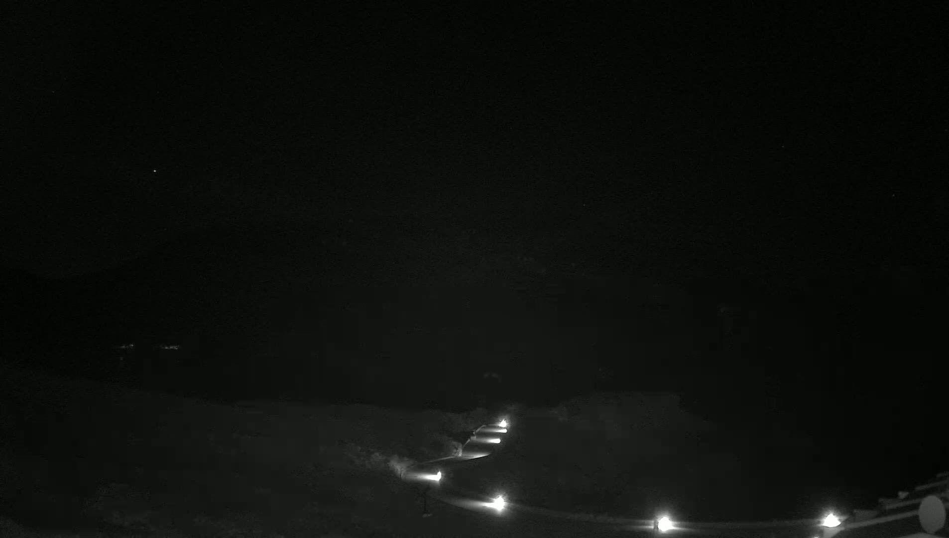 A snow-covered landscape at night is illuminated by a series of lights lining a winding path.