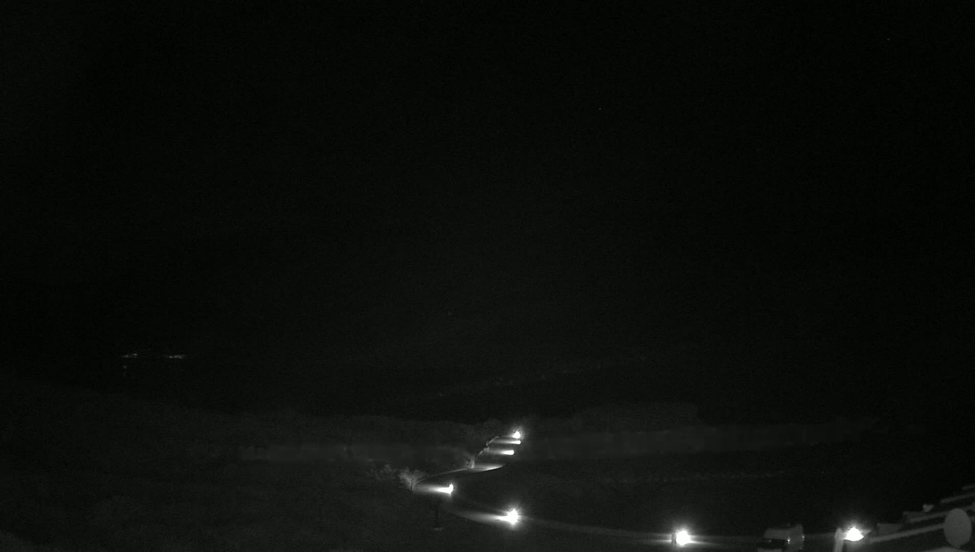 A dark, nighttime scene shows a winding road lit by a series of distant lights.