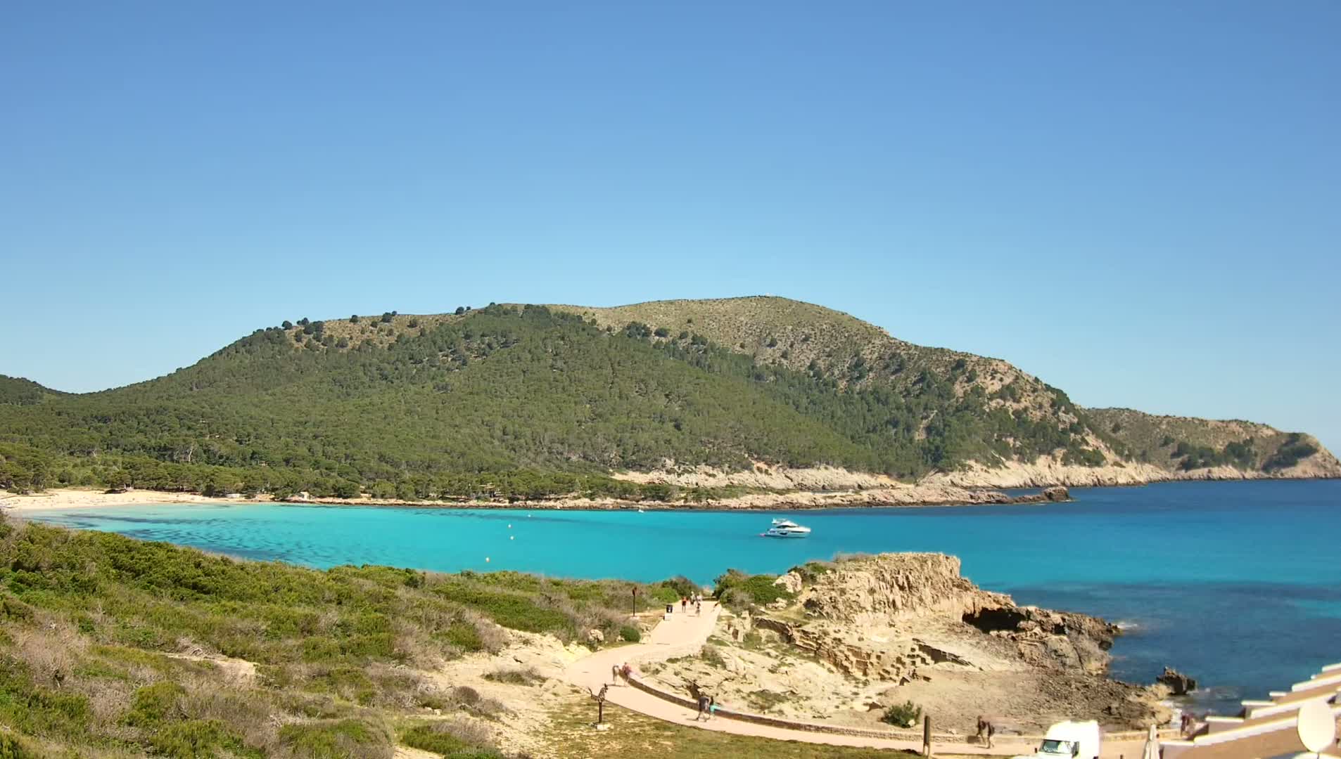 A secluded turquoise cove nestled beside a verdant hillside on a sunny day.