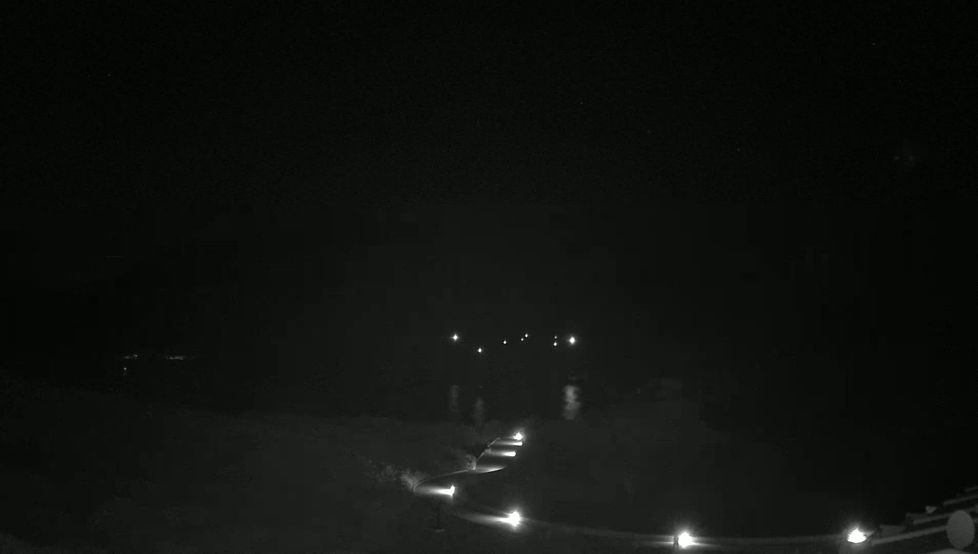 A winding path lit by spaced-out lamps is visible at night under a dark, clear sky.