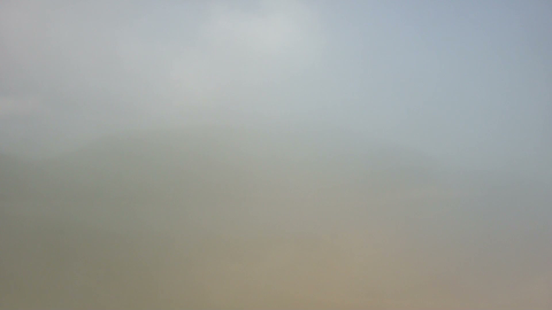 A very hazy outdoor landscape features a pale, indistinct sky blending into a slightly darker, brownish-grey ground, with extremely poor visibility.