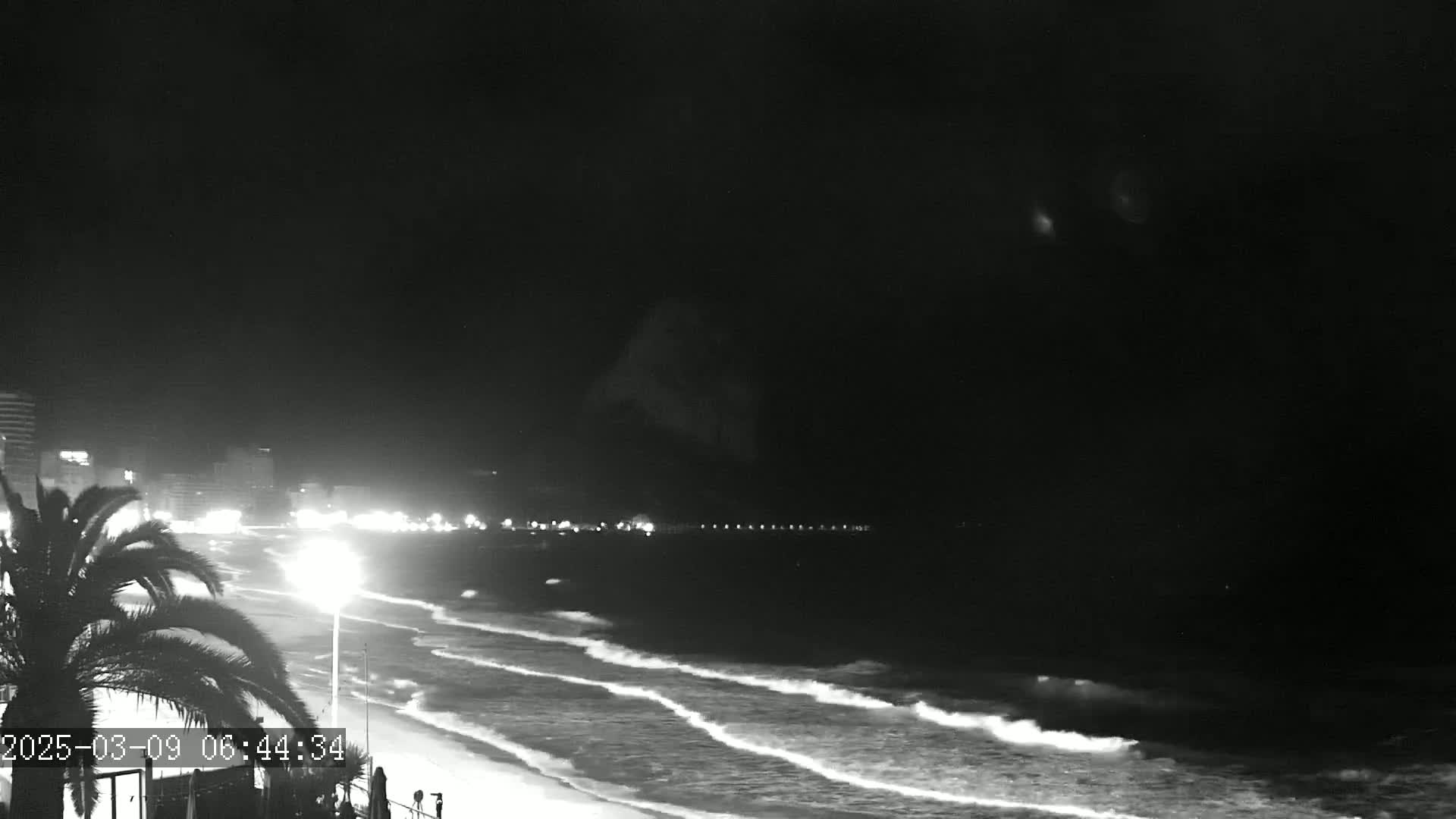 A nighttime beach scene shows gently rolling waves lapping the shore under a dark sky.