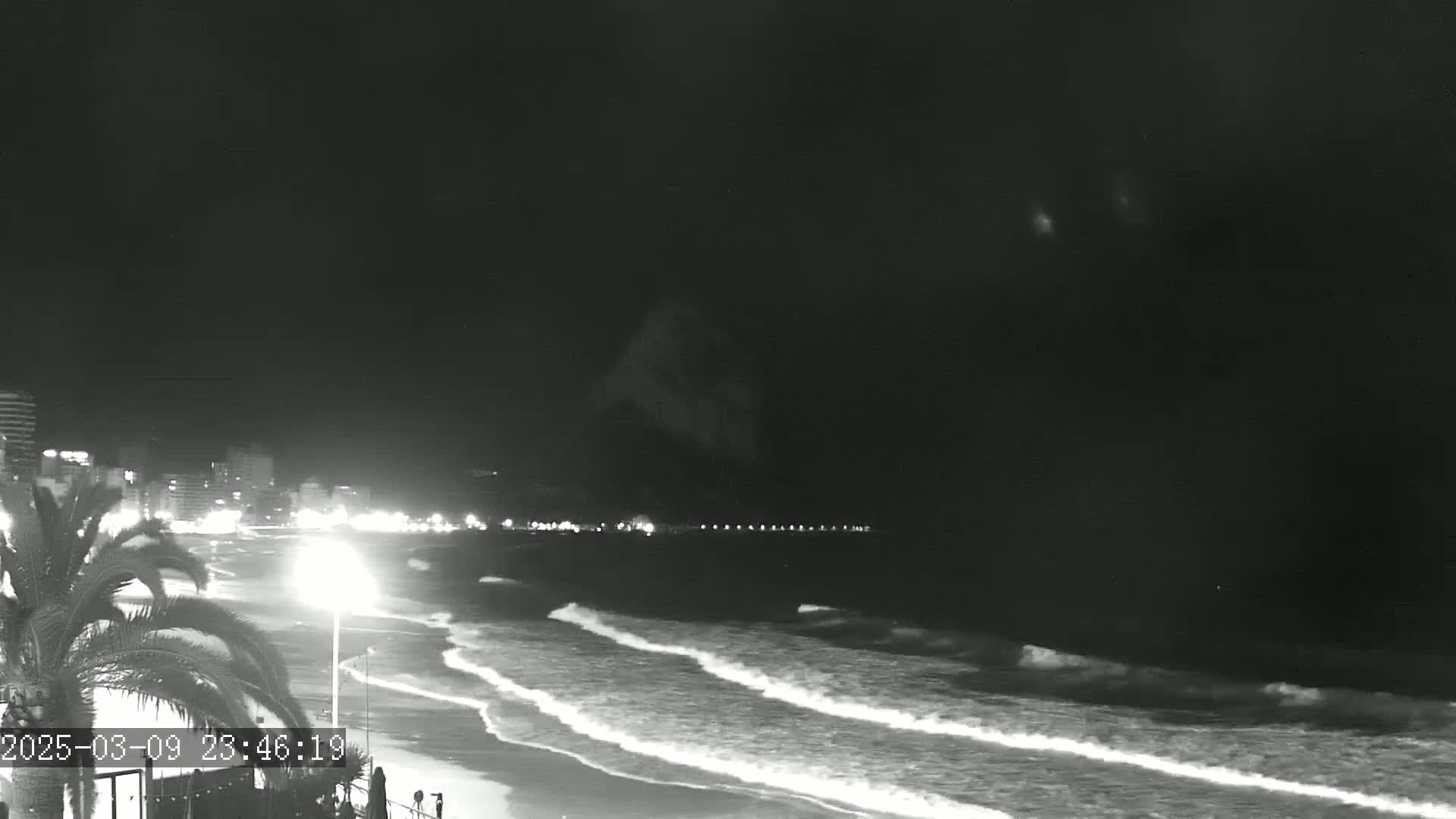 A nighttime beach scene shows gently rolling waves lapping the shore under a dark sky.