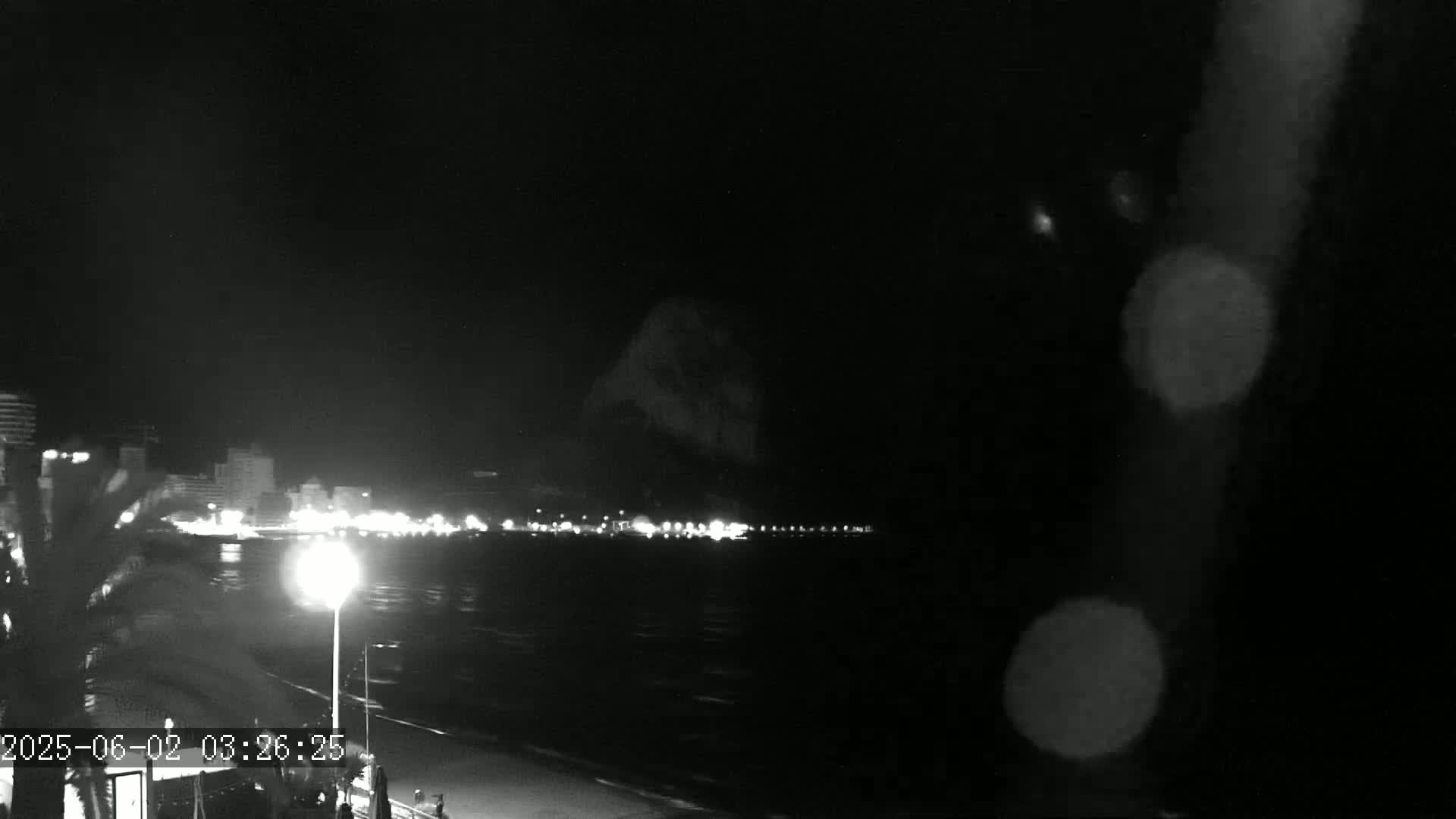 A nighttime, blurry view of a city skyline across a body of water, under a dark sky with rain or water droplets on the lens.