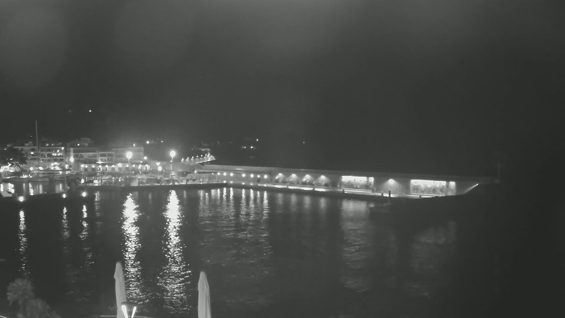 A nighttime view of a calm harbor with a long, illuminated waterfront structure and buildings across the water.