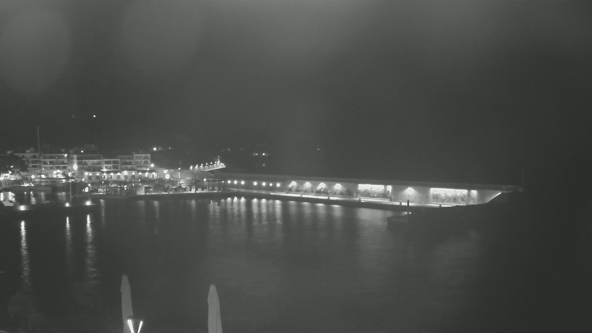 A nighttime view of a calm harbor with illuminated buildings and a long, light-lined structure along the water.