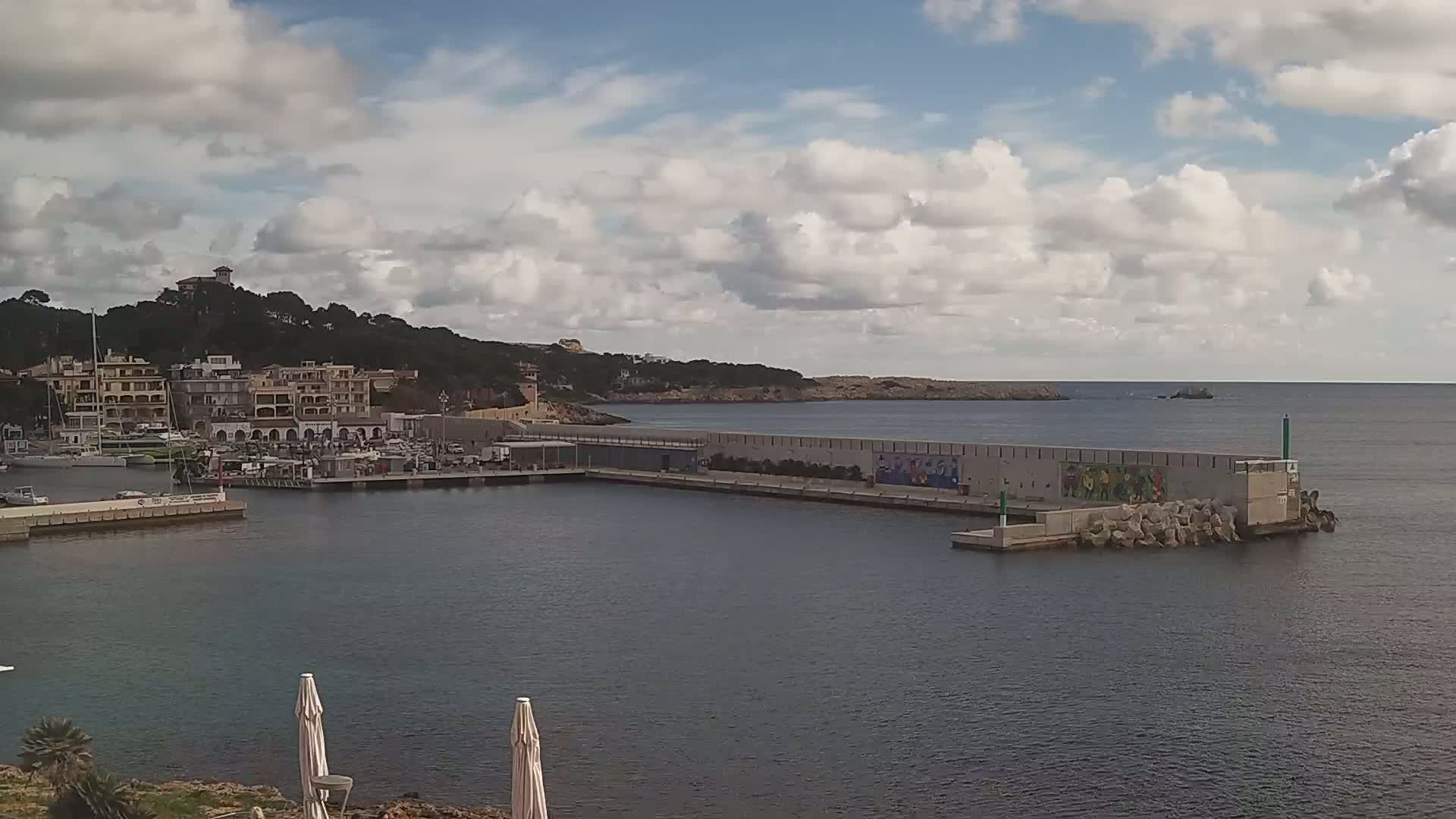 A harbor filled with boats sits below a hillside town under a partly cloudy sky.