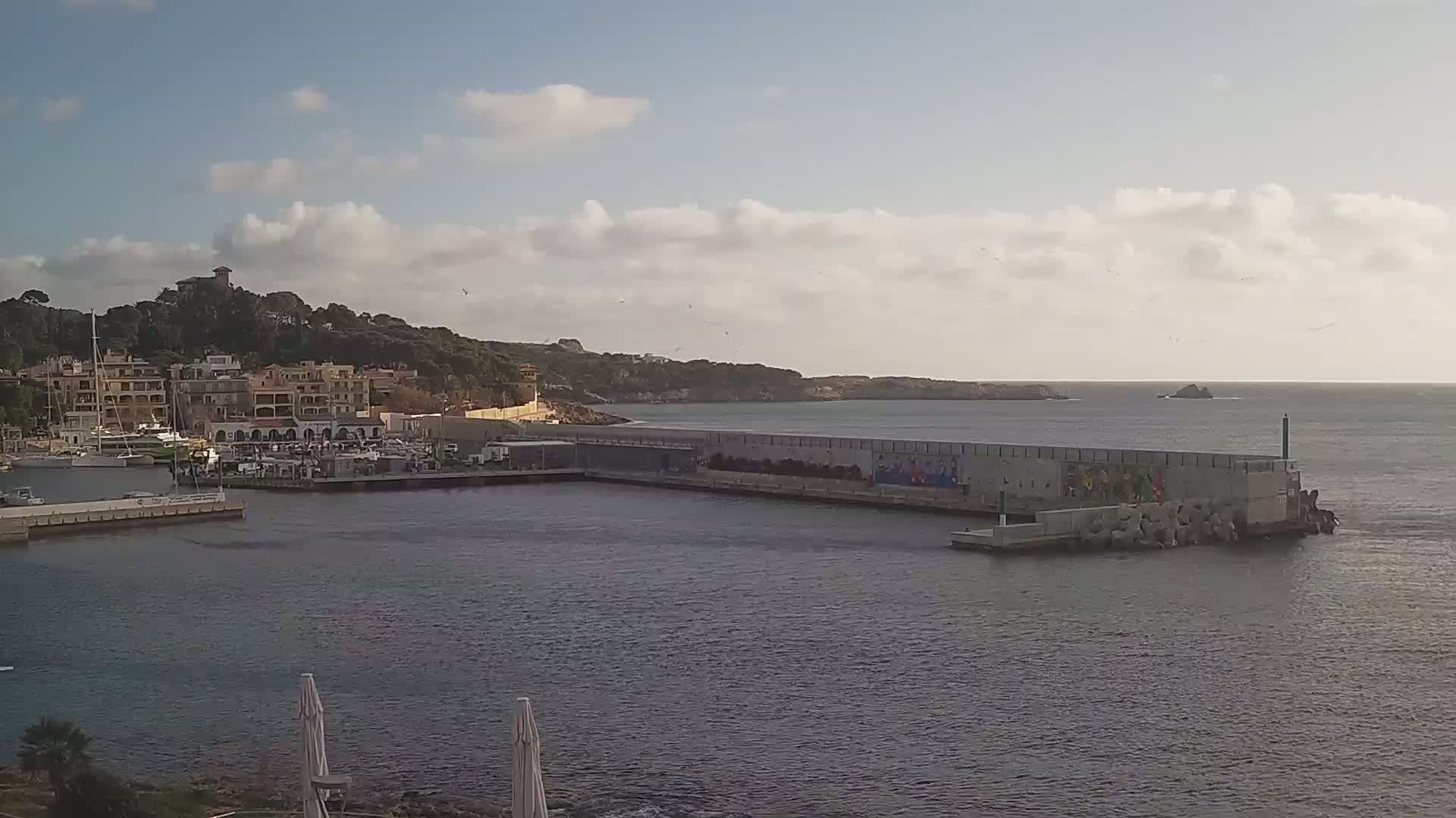 A harbor with boats, buildings, and a seawall under a partly cloudy sky.