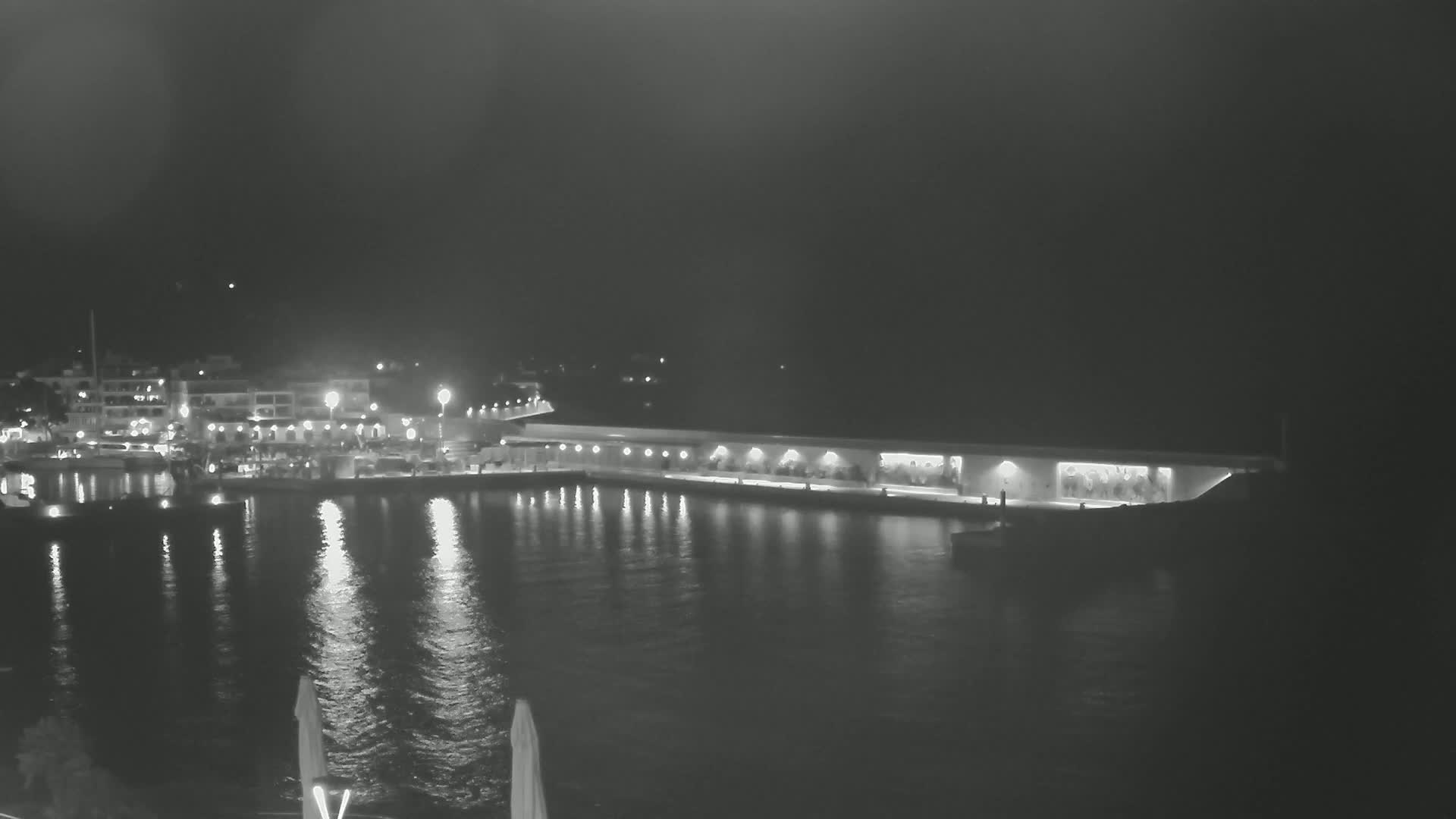 A nighttime view of a harbor with boats and buildings, illuminated by lights reflecting on calm water.