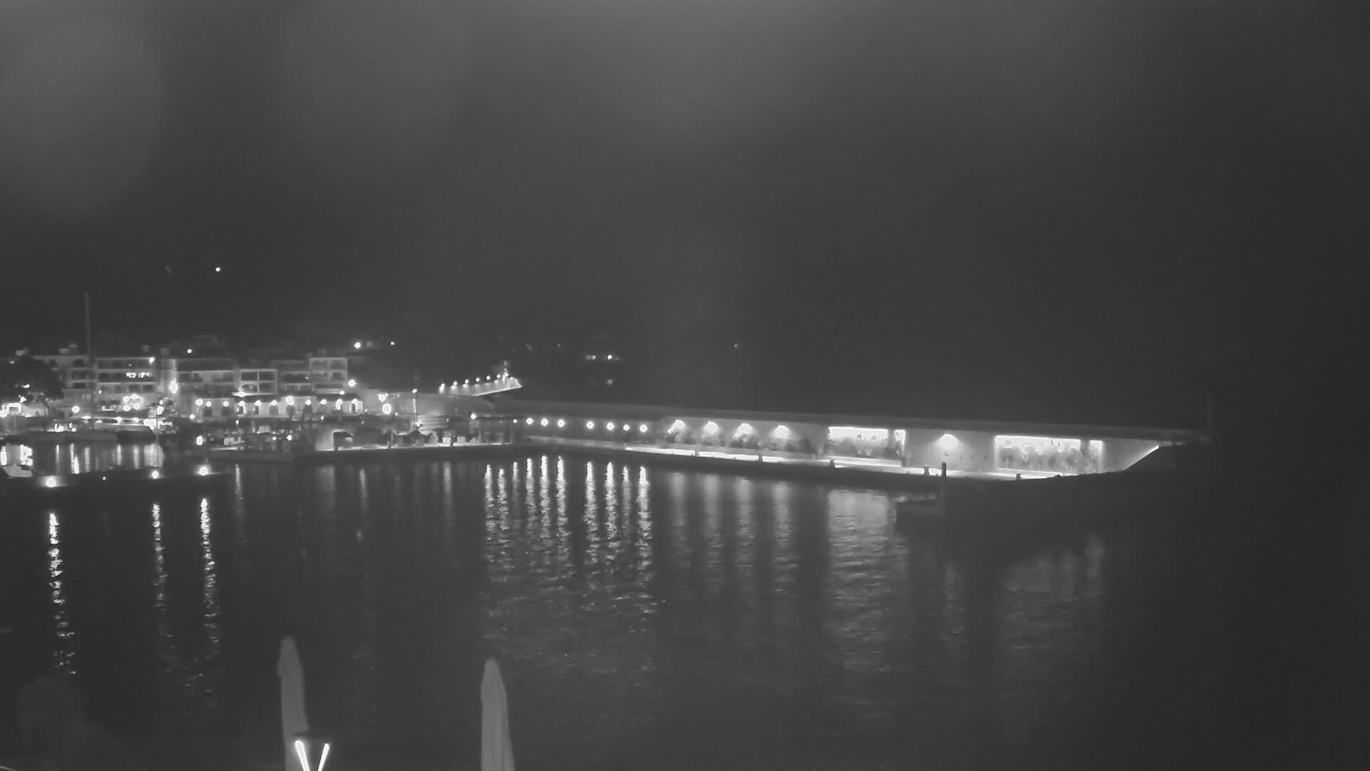 A nighttime view of a harbor with boats and buildings illuminated along a calm waterfront.