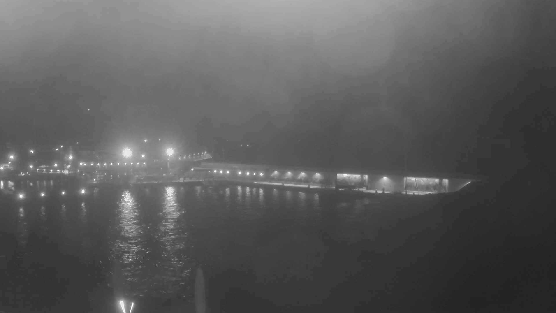 A long, low building is illuminated at night along a waterway shrouded in thick fog.