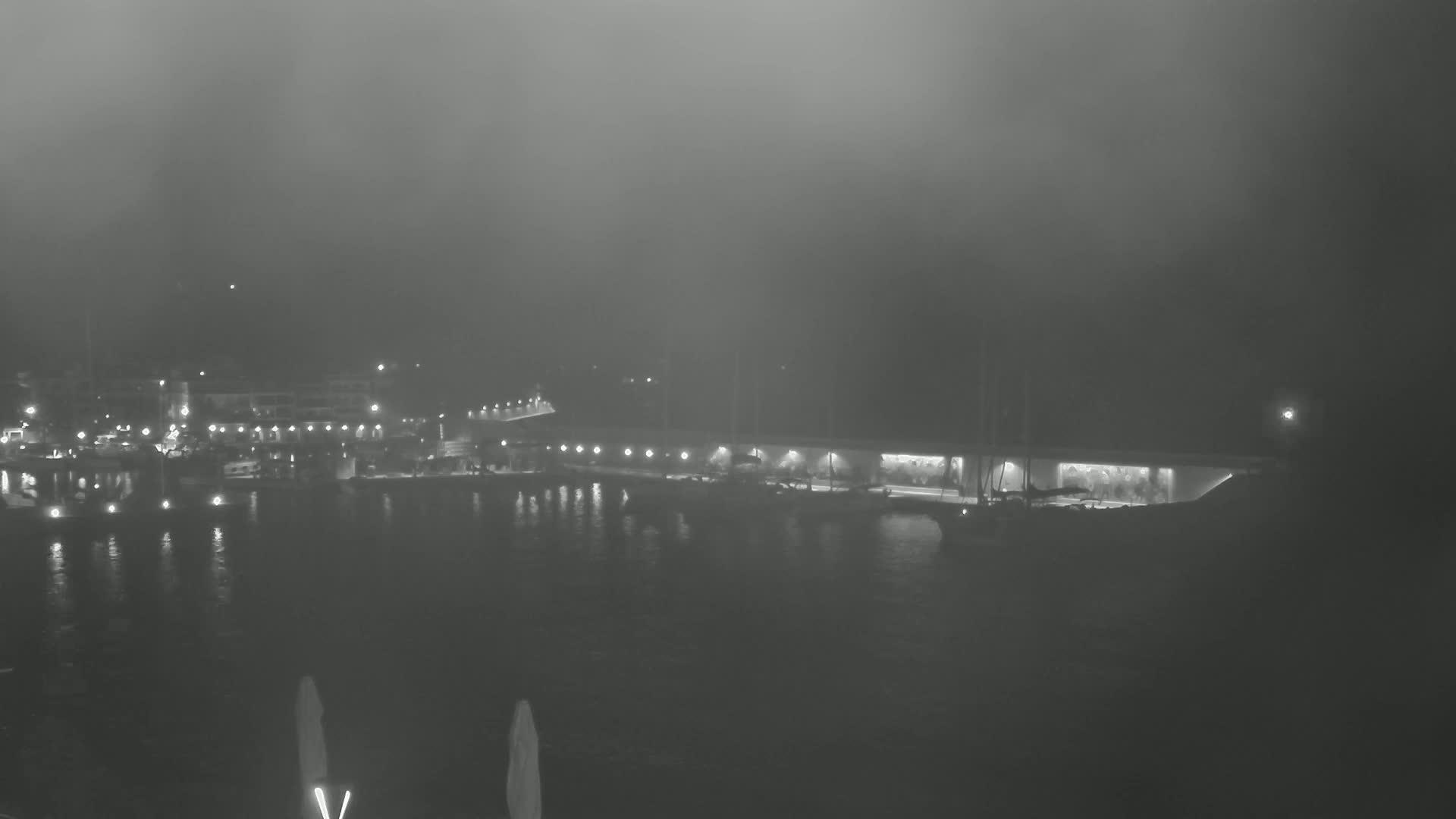 A foggy night scene shows a harbor with boats and buildings faintly illuminated along the waterfront.