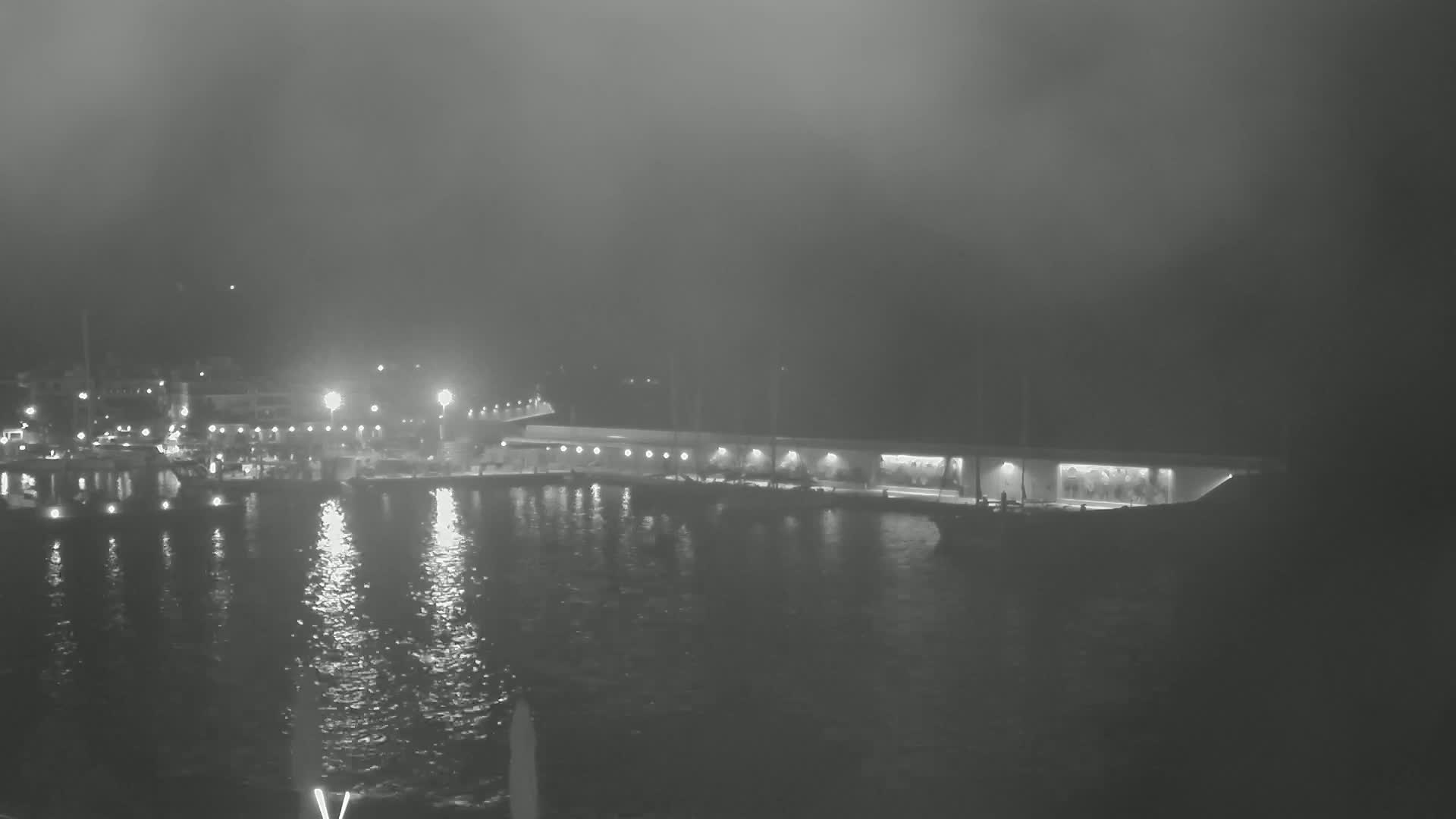 A foggy night scene shows a harbor with boats and lights reflecting on the water.
