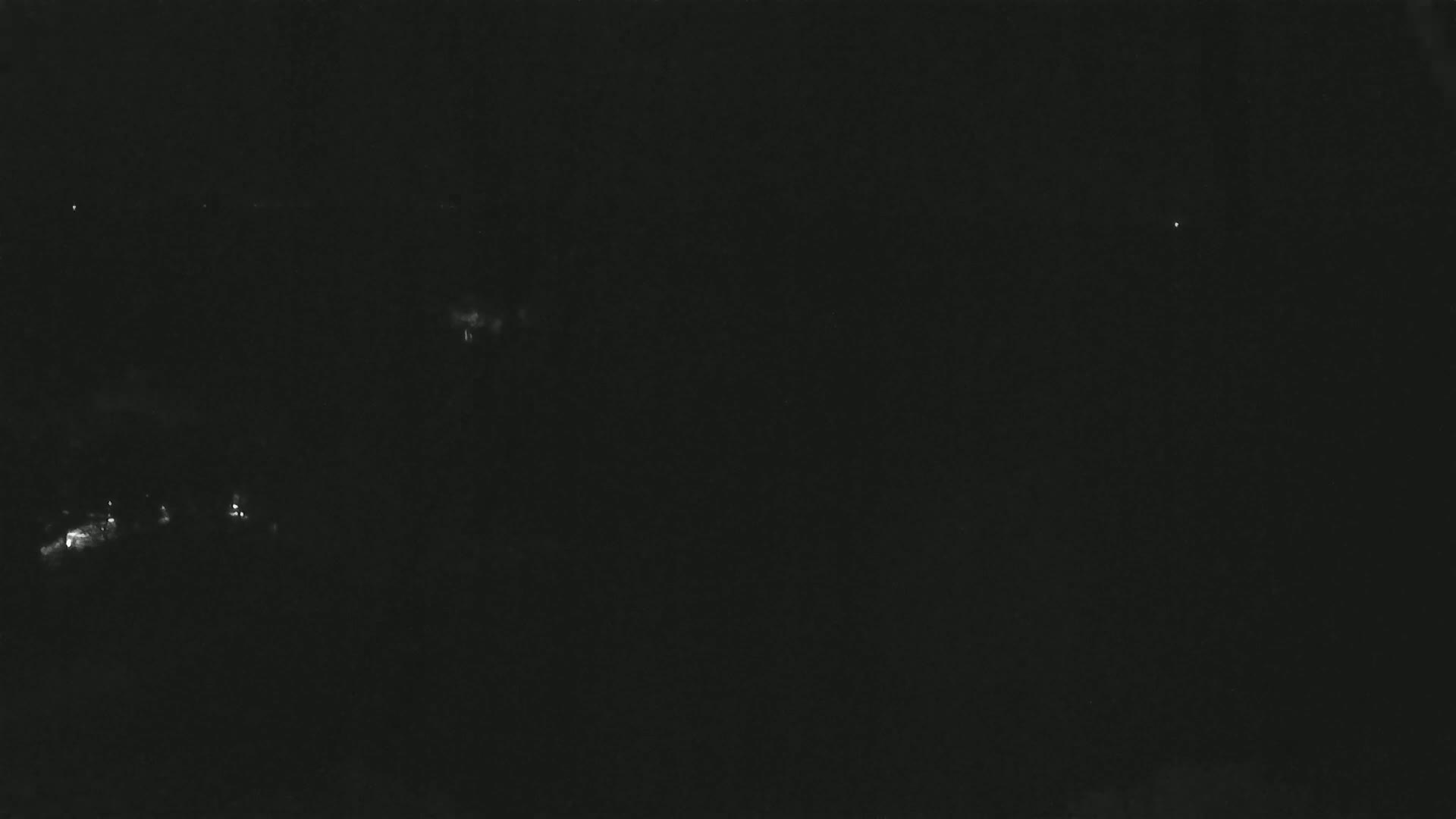 A dark, nighttime scene shows a few faint lights in the distance.