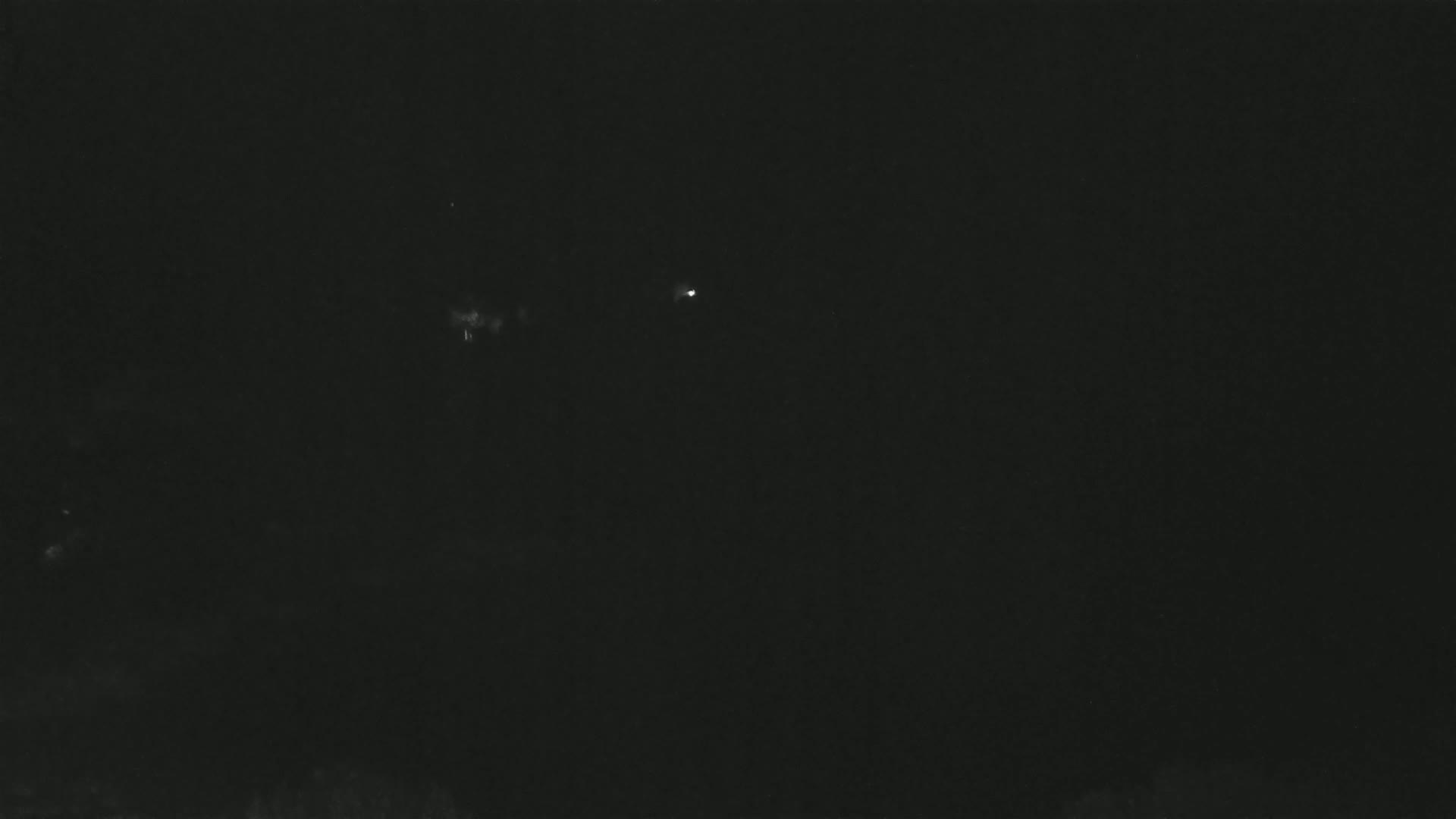 A dark, nighttime scene shows a few faint lights in the distance against a mostly black sky.
