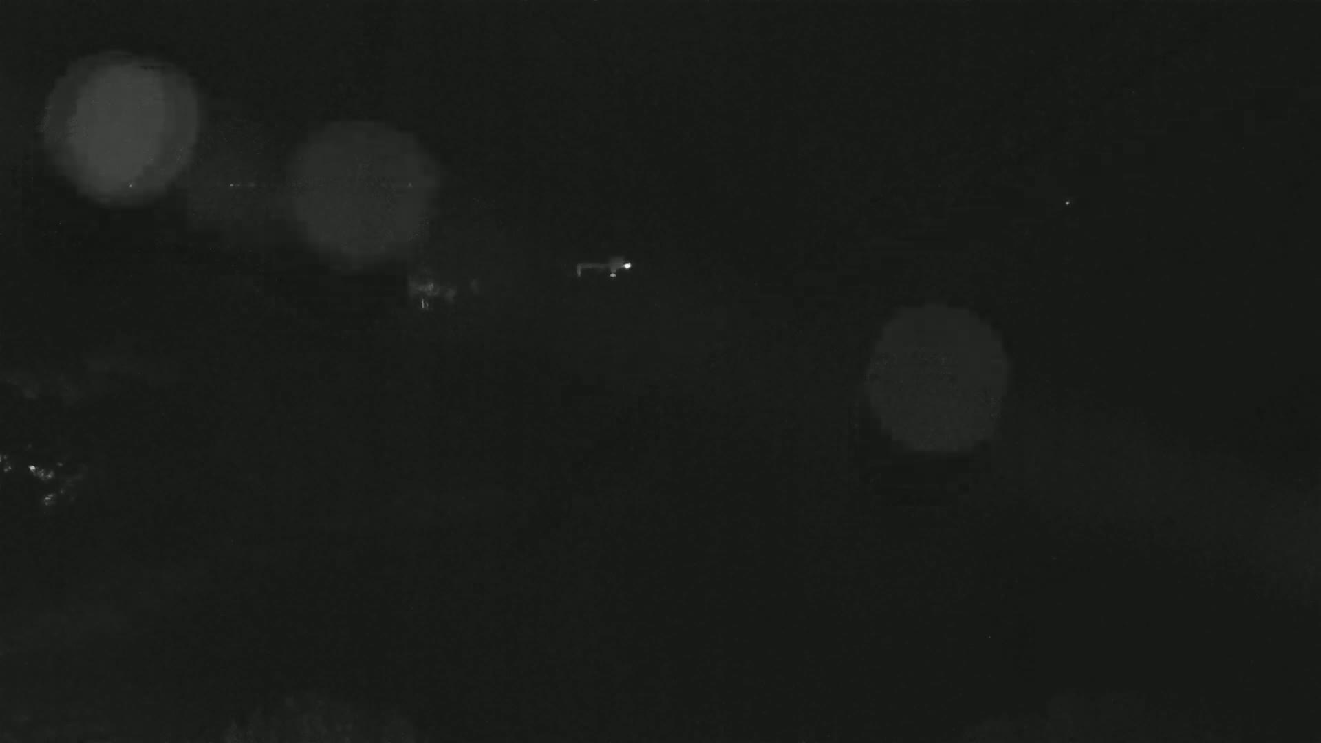 A dark, nighttime scene shows blurry lights in the distance and a very faint, possibly distant object.