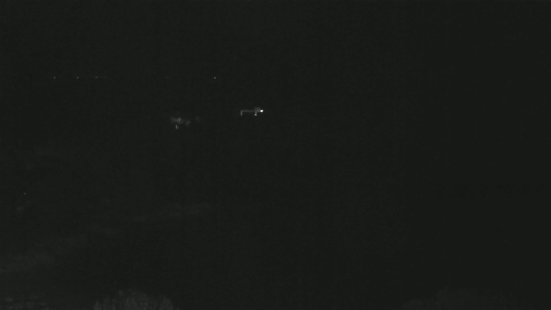 A dark, nighttime scene shows a few faint lights in the distance.