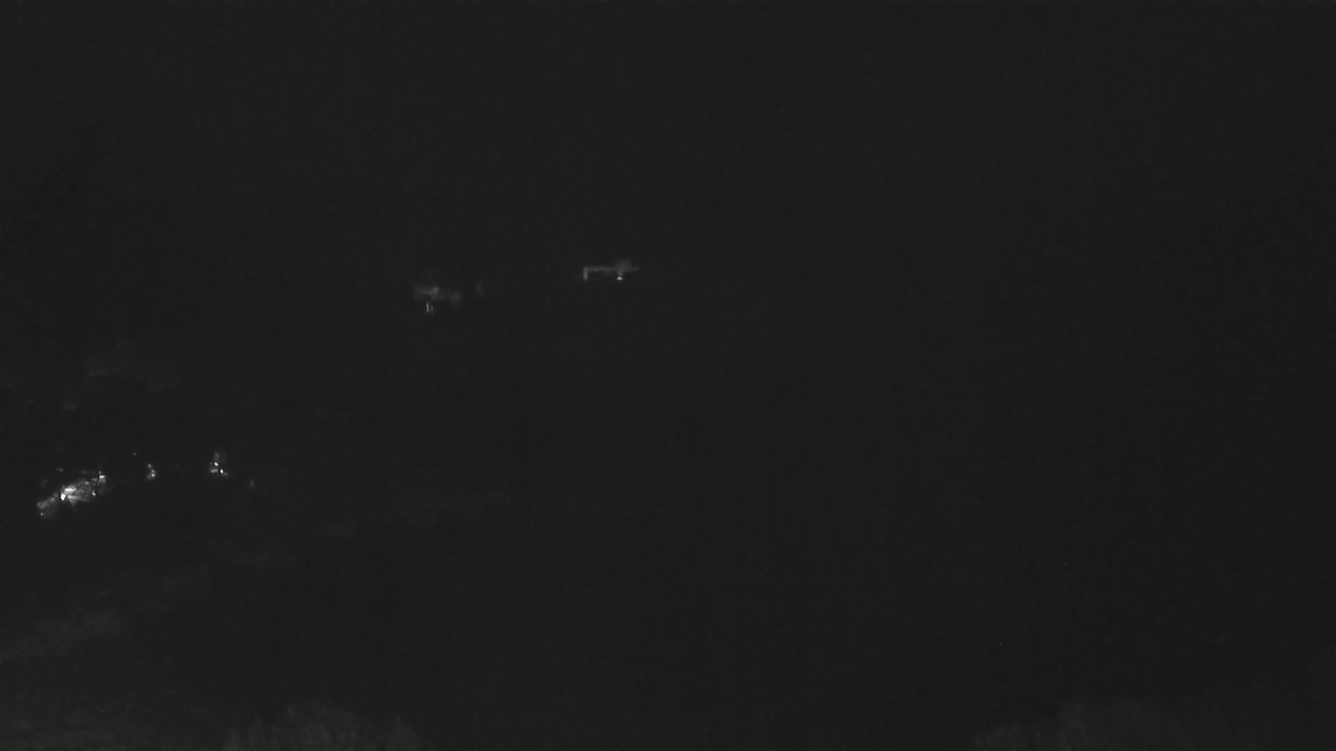A nighttime, long-range view shows faint lights from a distant town or settlement under a dark sky.
