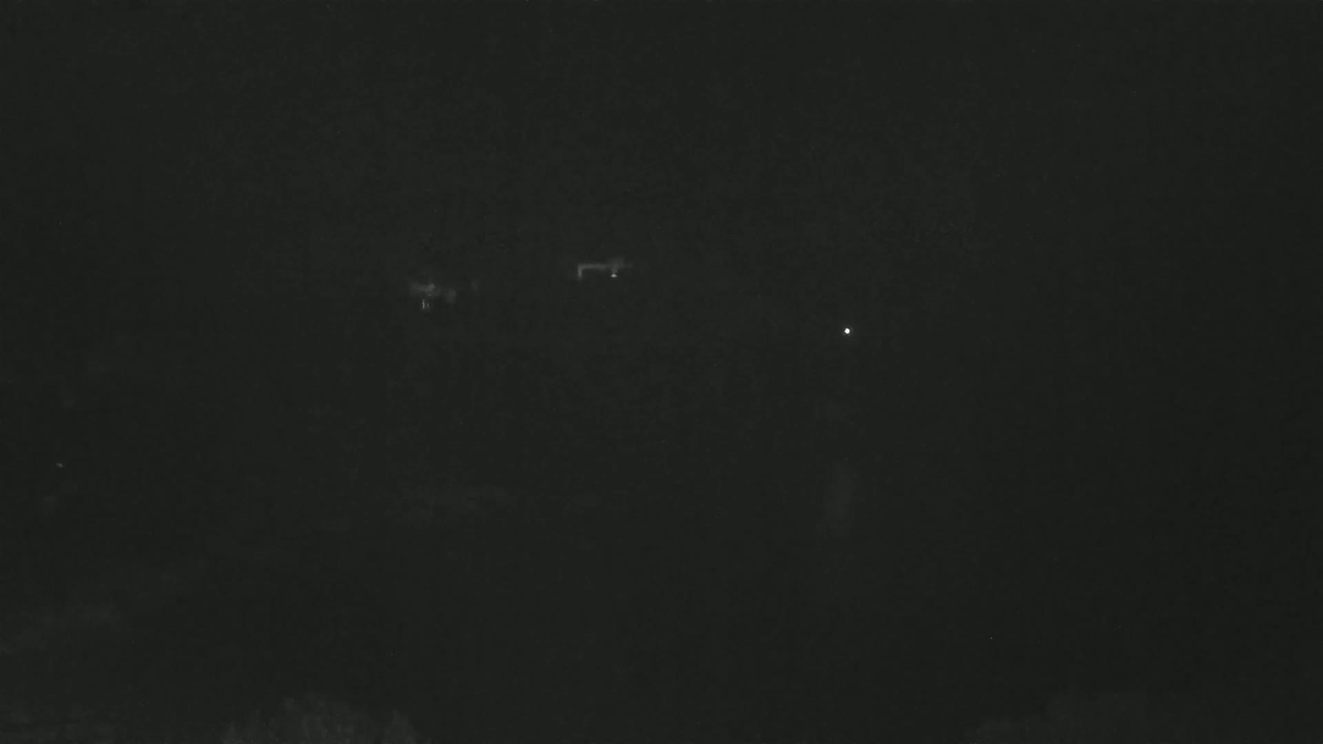 A dark, nighttime scene shows a few faint lights in the distance.