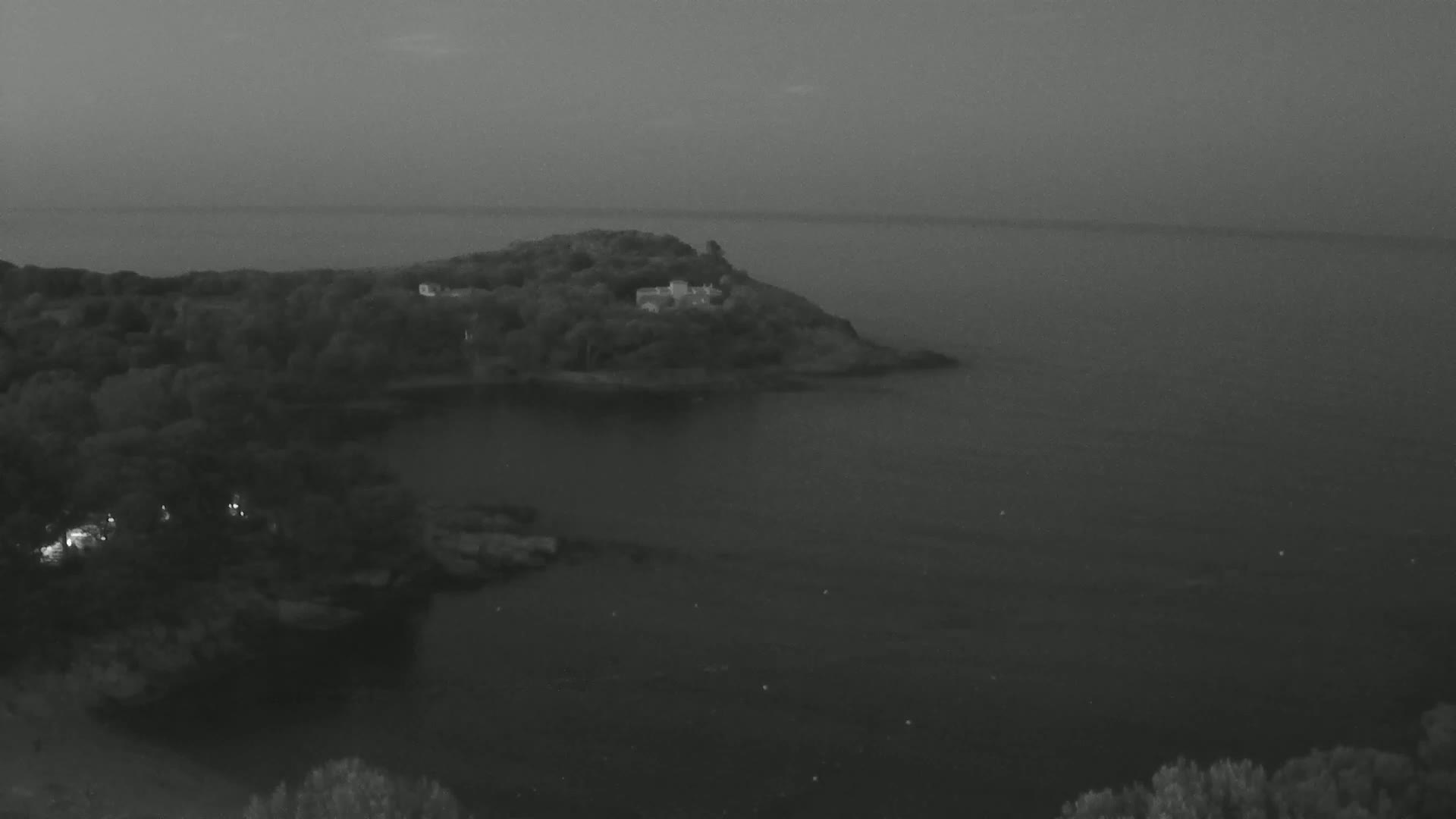 A small, tree-covered island with a building on it sits in a dark, calm body of water under a dusky sky.
