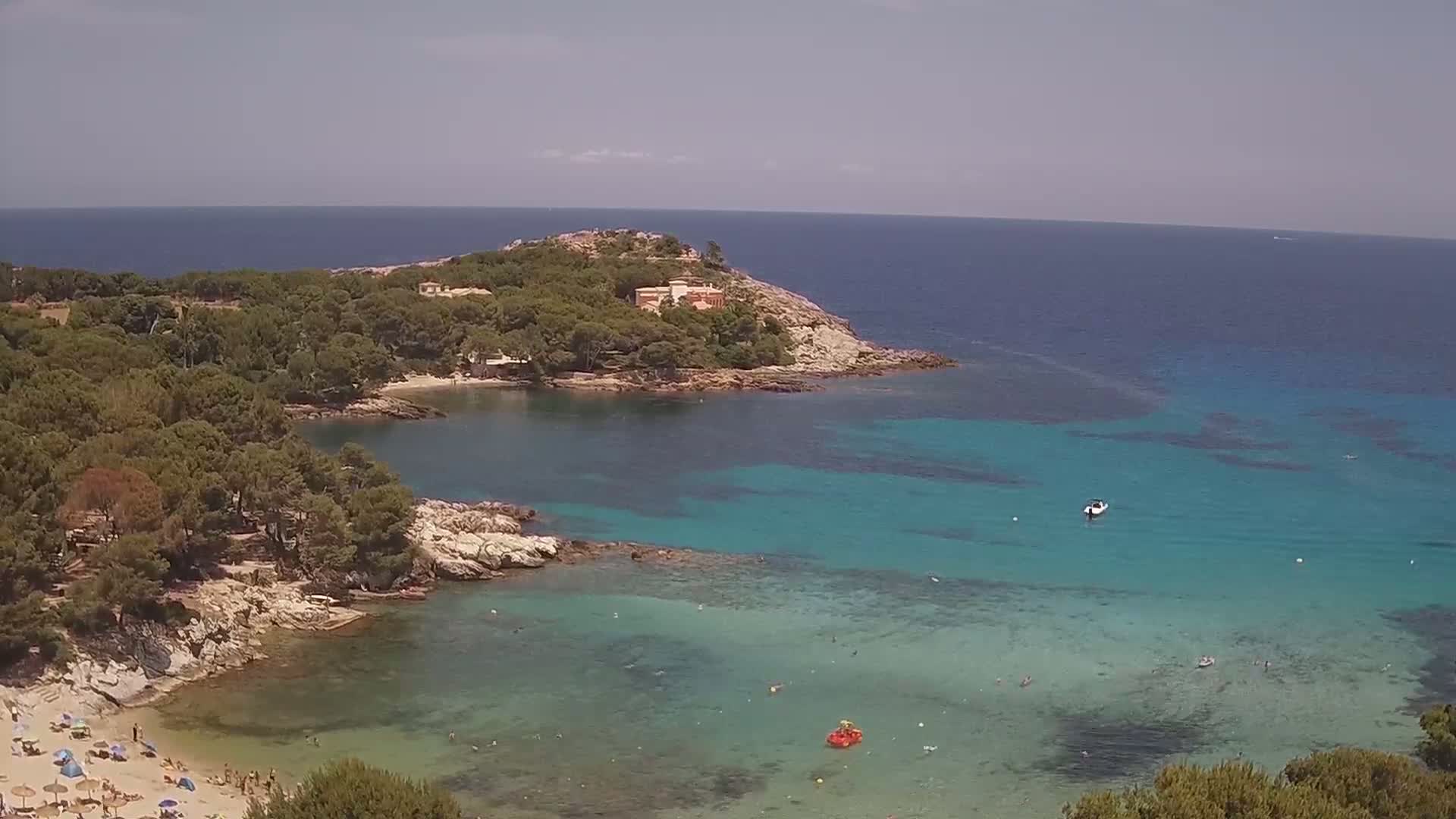 A secluded cove with a sandy beach, surrounded by lush green trees and clear turquoise water under a sunny sky.