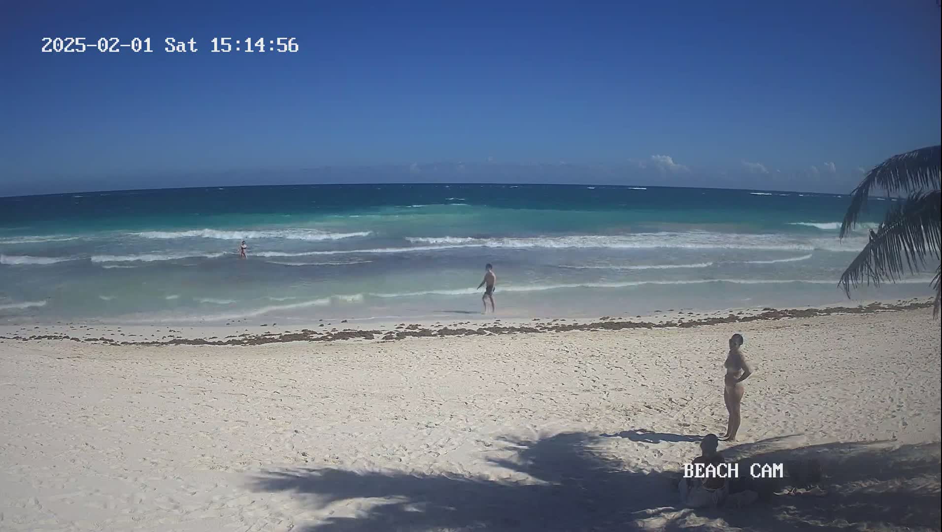 A white sandy beach with a few people, some in the turquoise water and others on the shore, under a clear blue sky.
