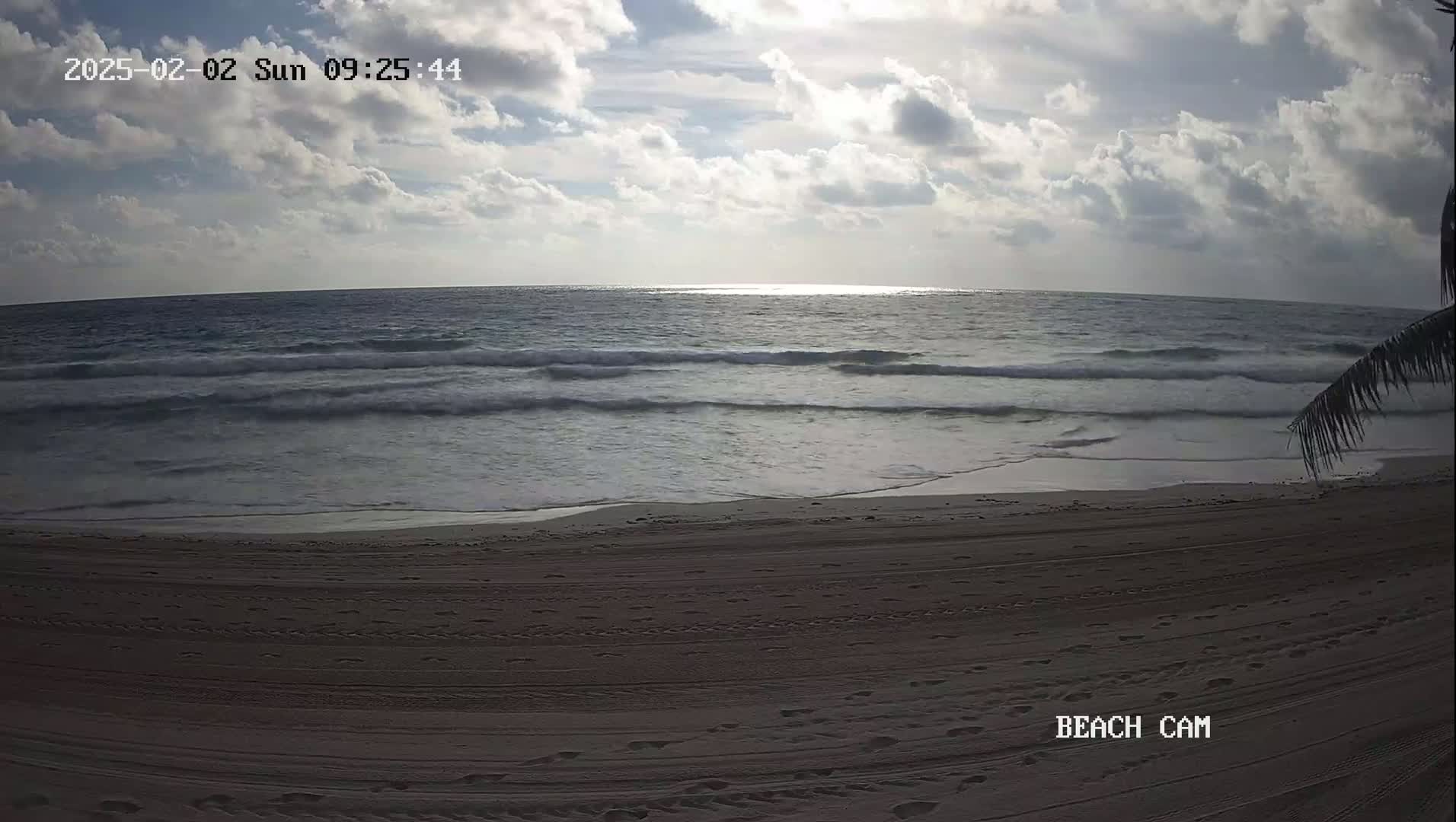 A partly cloudy sky brightens a sandy beach where gentle waves lap the shore under a partly cloudy sky.