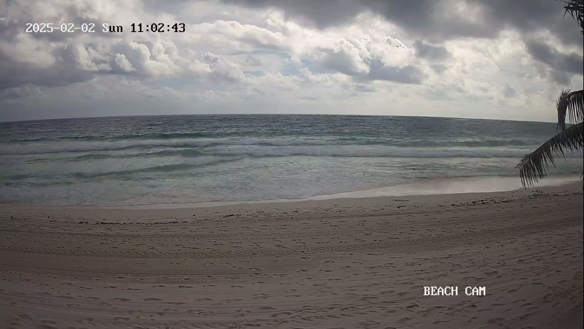 A sandy beach with footprints stretches to a calm ocean under a cloudy sky.