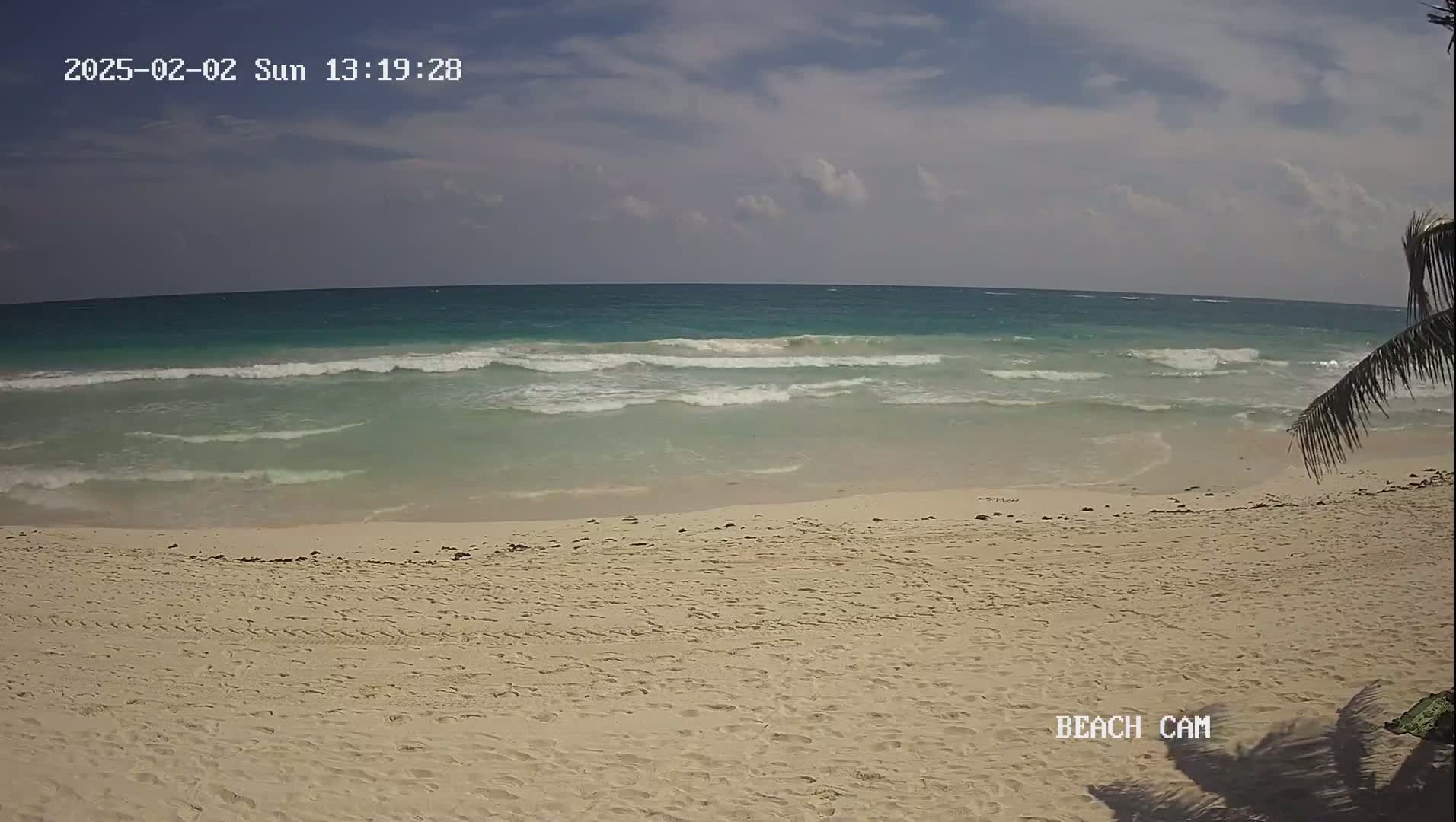 A sandy beach with small waves under a partly cloudy sky is shown.