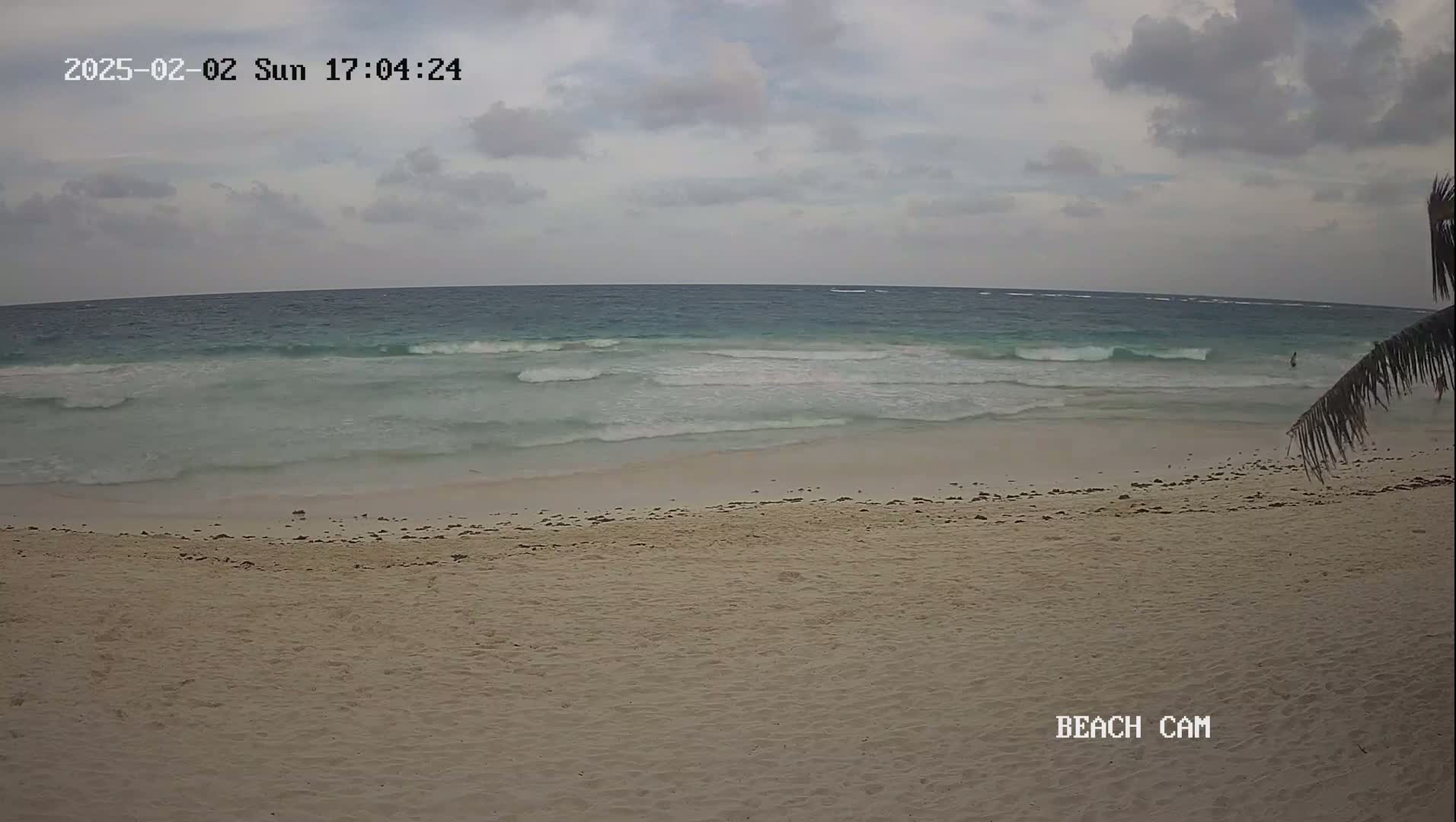 A sandy beach with small waves rolling onto the shore under an overcast sky.