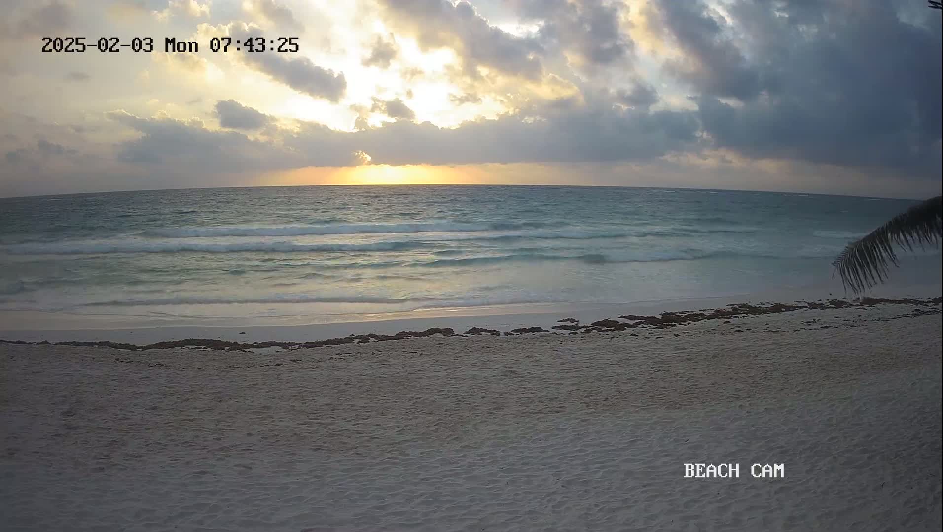 A sandy beach with gentle waves under a cloudy sunrise sky.