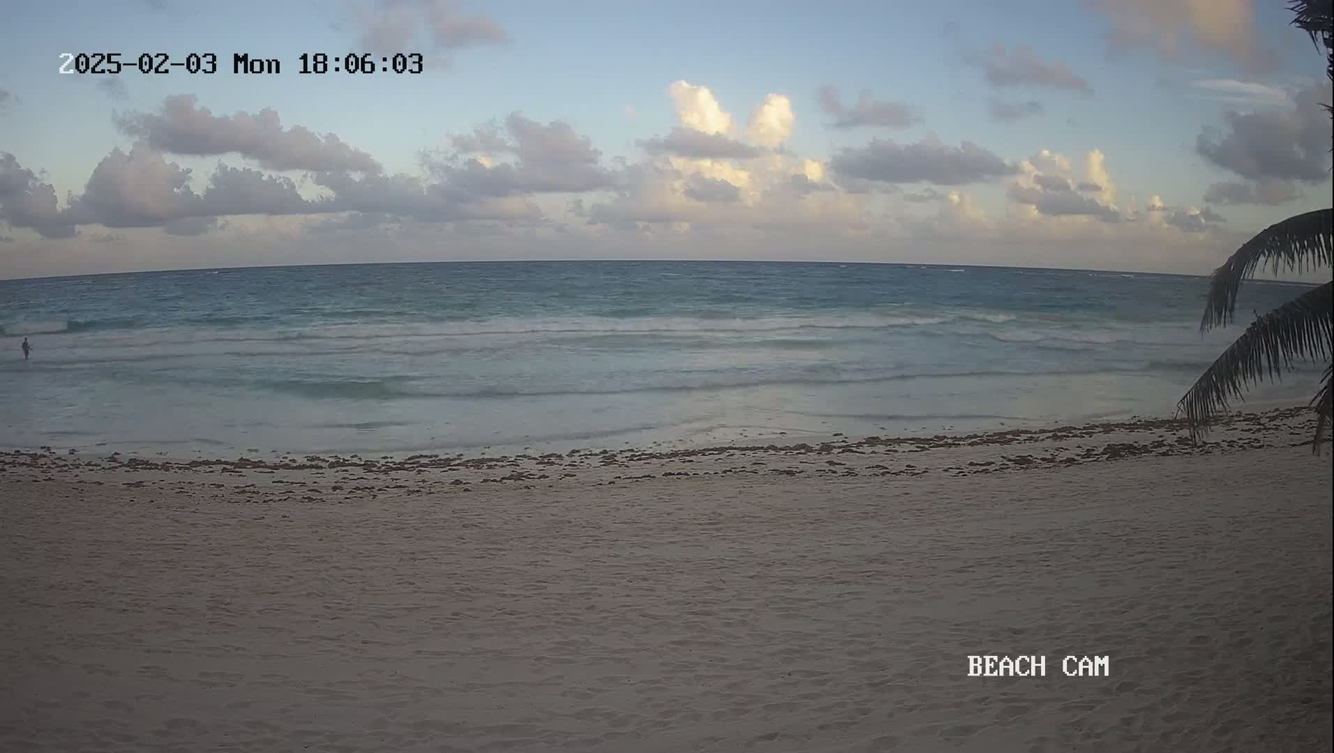 A sandy beach with gentle waves under a partly cloudy sky.