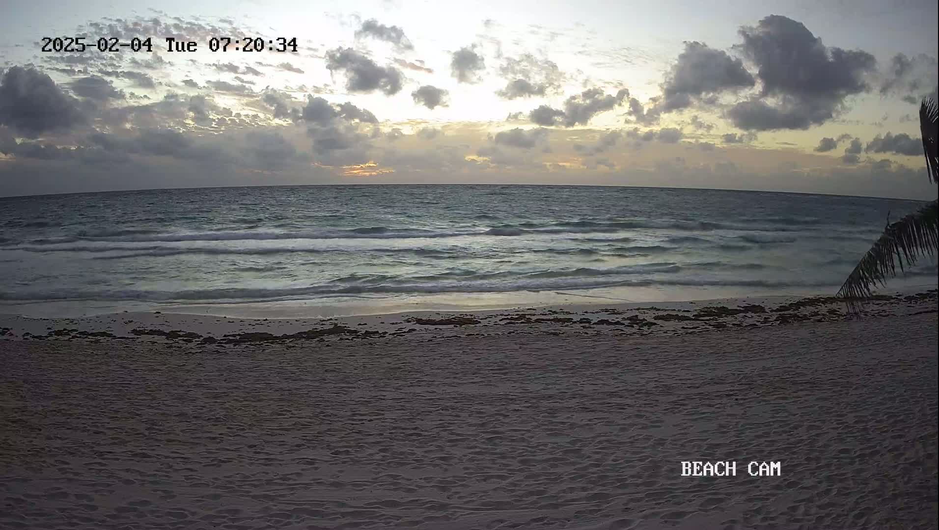 A sandy beach with gentle waves under a cloudy sunrise sky.
