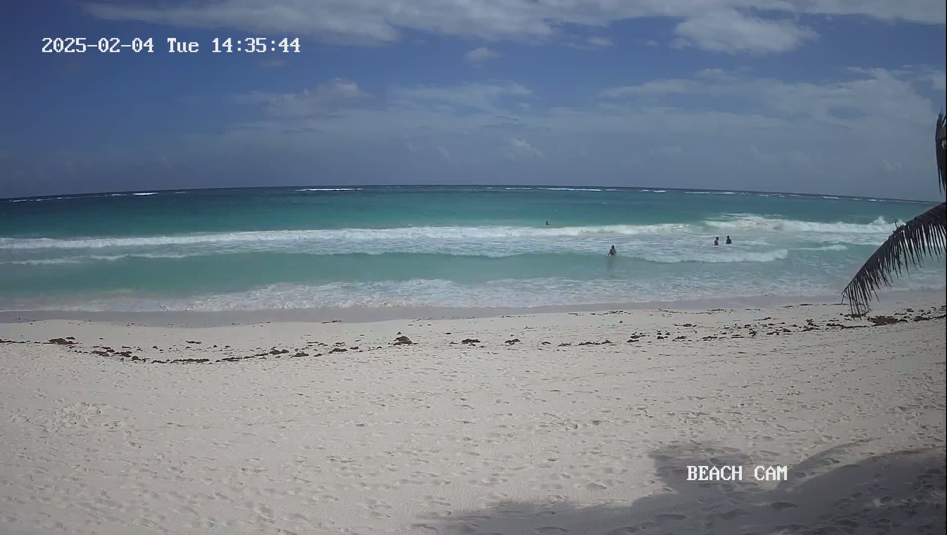 A mostly sunny day shows a white sand beach with turquoise water and small waves; several people are swimming in the ocean.