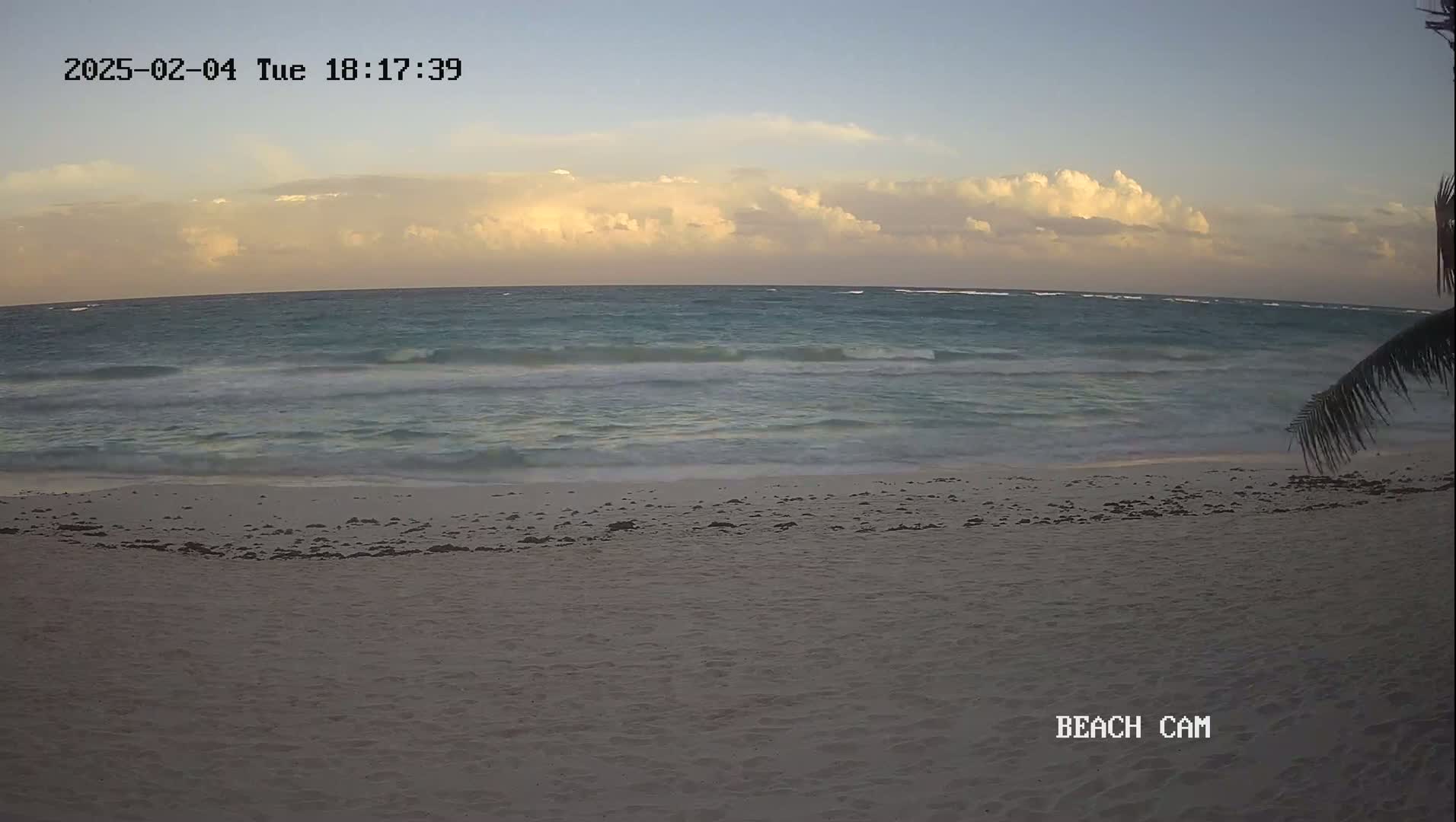 A sandy beach with gentle waves under a partly cloudy, twilight sky.