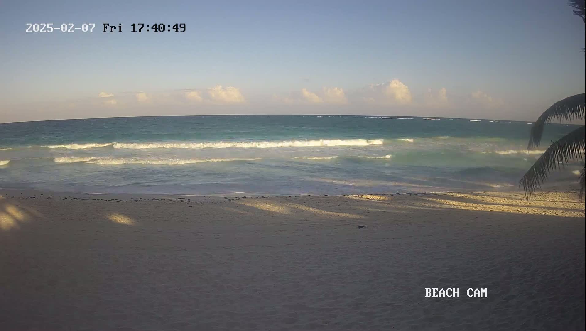 A sandy beach with gentle waves lapping the shore under a partly cloudy sky.
