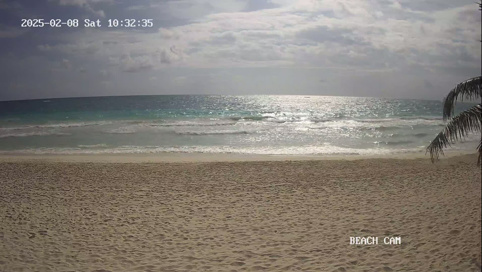A sandy beach with gentle waves under a partly cloudy sky.