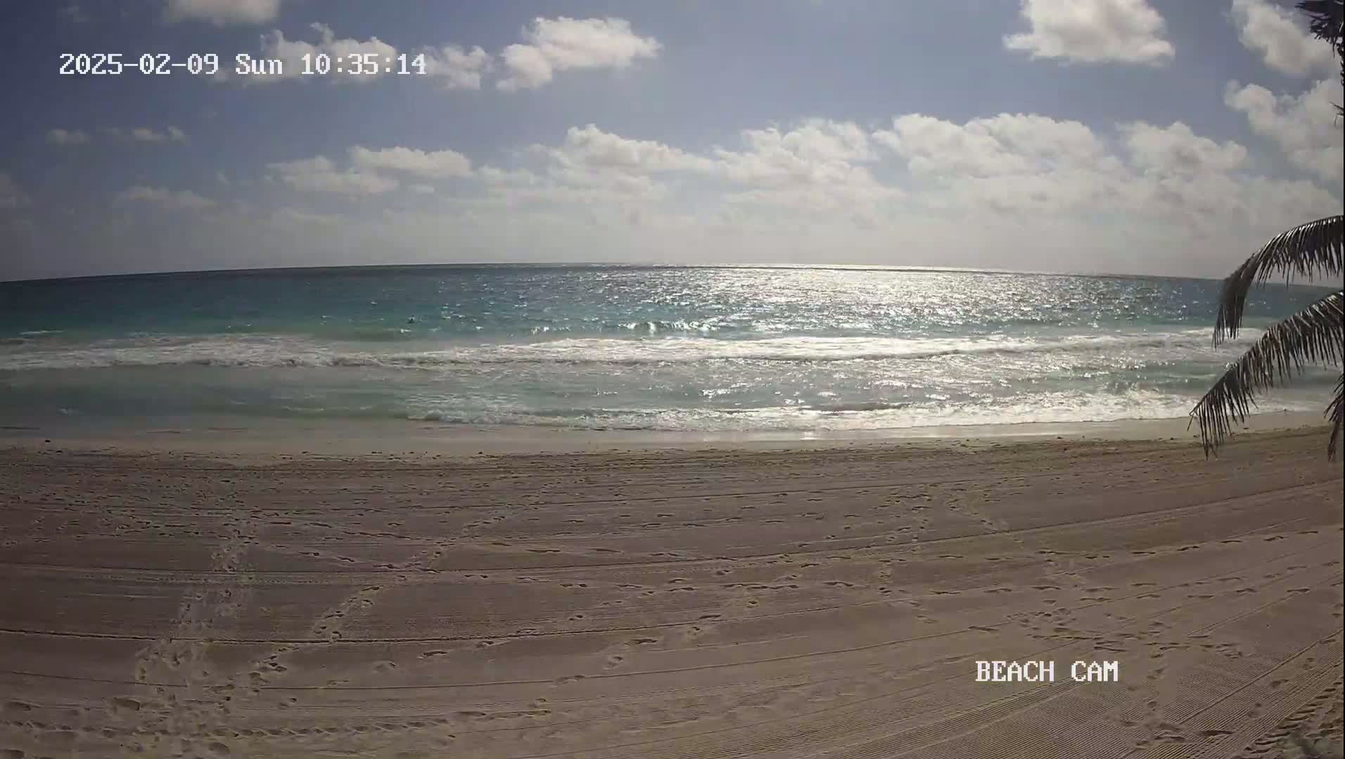 A sandy beach with gentle waves under a partly sunny sky.