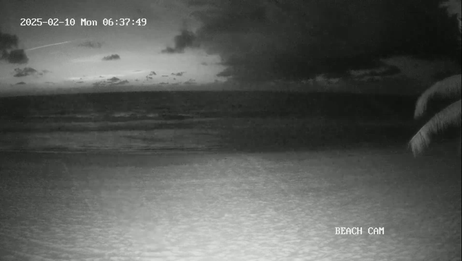 A dark, cloudy night scene shows a beach with a calm ocean under a partly cloudy sky.