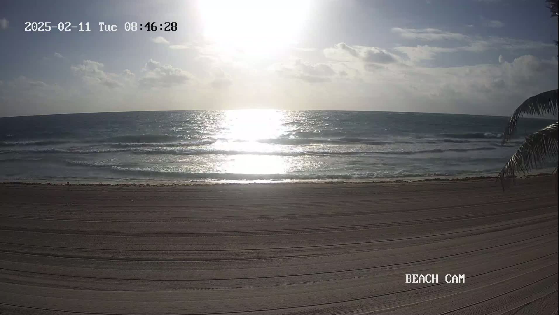 A sandy beach with gentle waves under a partly cloudy, sunny sky.