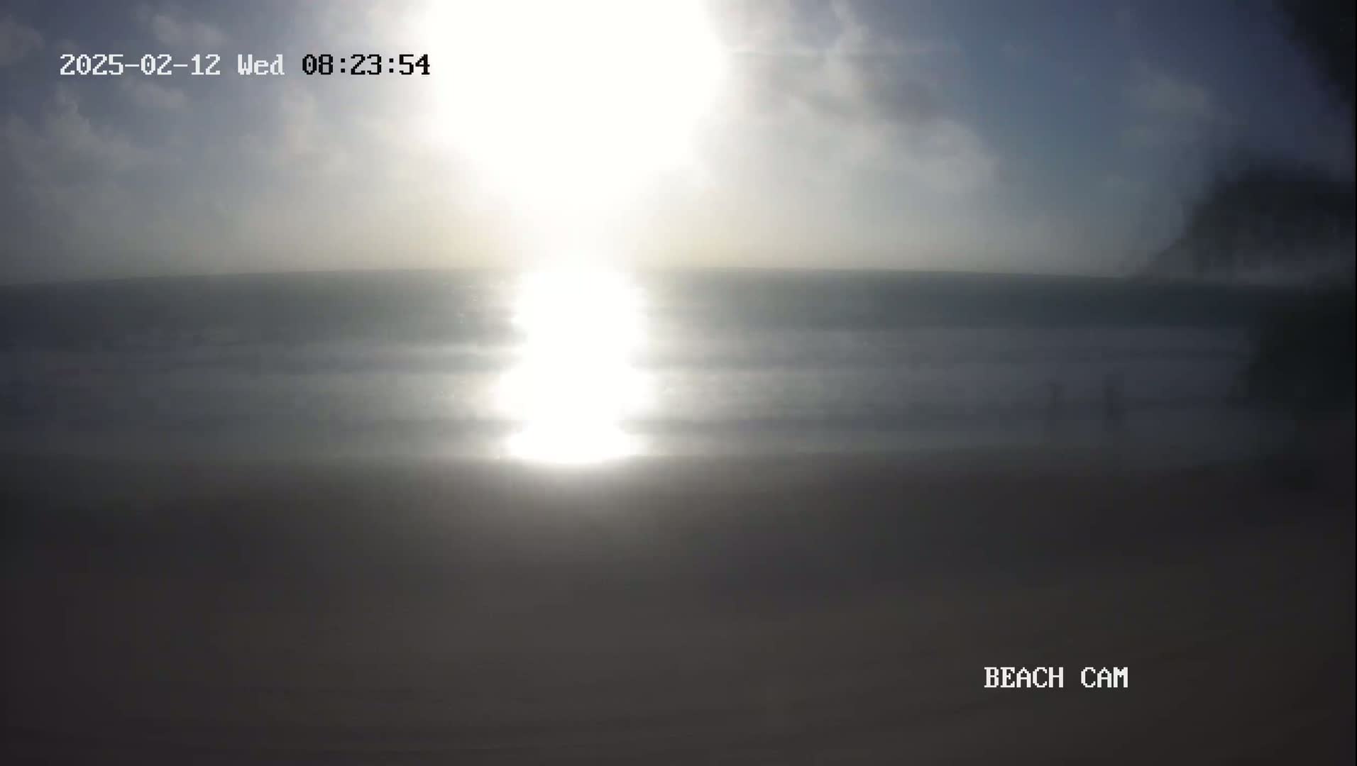 A hazy, bright sunrise over a beach with calm waves.