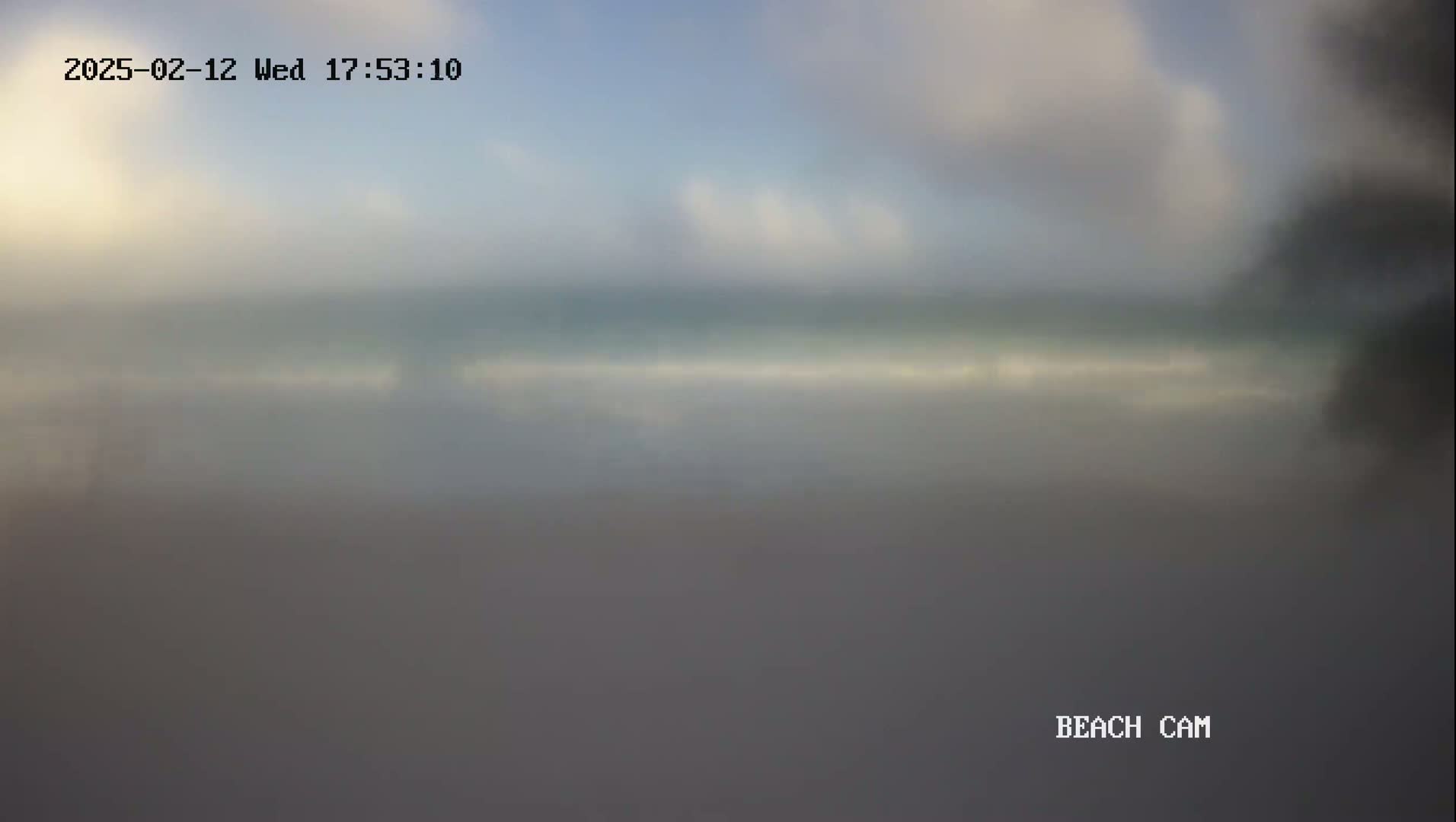 A hazy, overcast view shows a beach and ocean under a cloudy sky.